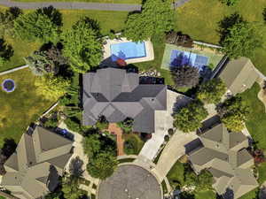 Aerial perspective showcasing a multi-gabled residence with an expansive private pool, sport court, mature trees, and circular driveway