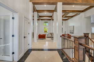 Entryway featuring coffered ceilings with exposed wood beams, a staircase with wood newel posts and wrought iron balusters, and a tiled floor with contrasting black and light-toned tiles