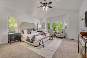 Vaulted ceiling with a ceiling fan, bay window seating area, plantation shutters, neutral-toned carpeting, and an upholstered bed frame