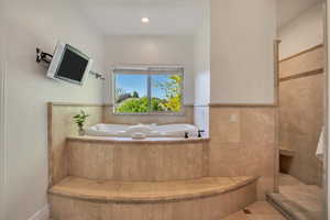 Jetted soaking tub set within a tiled surround, featuring a window and an adjacent walk-in shower with a built-in bench and tile accents