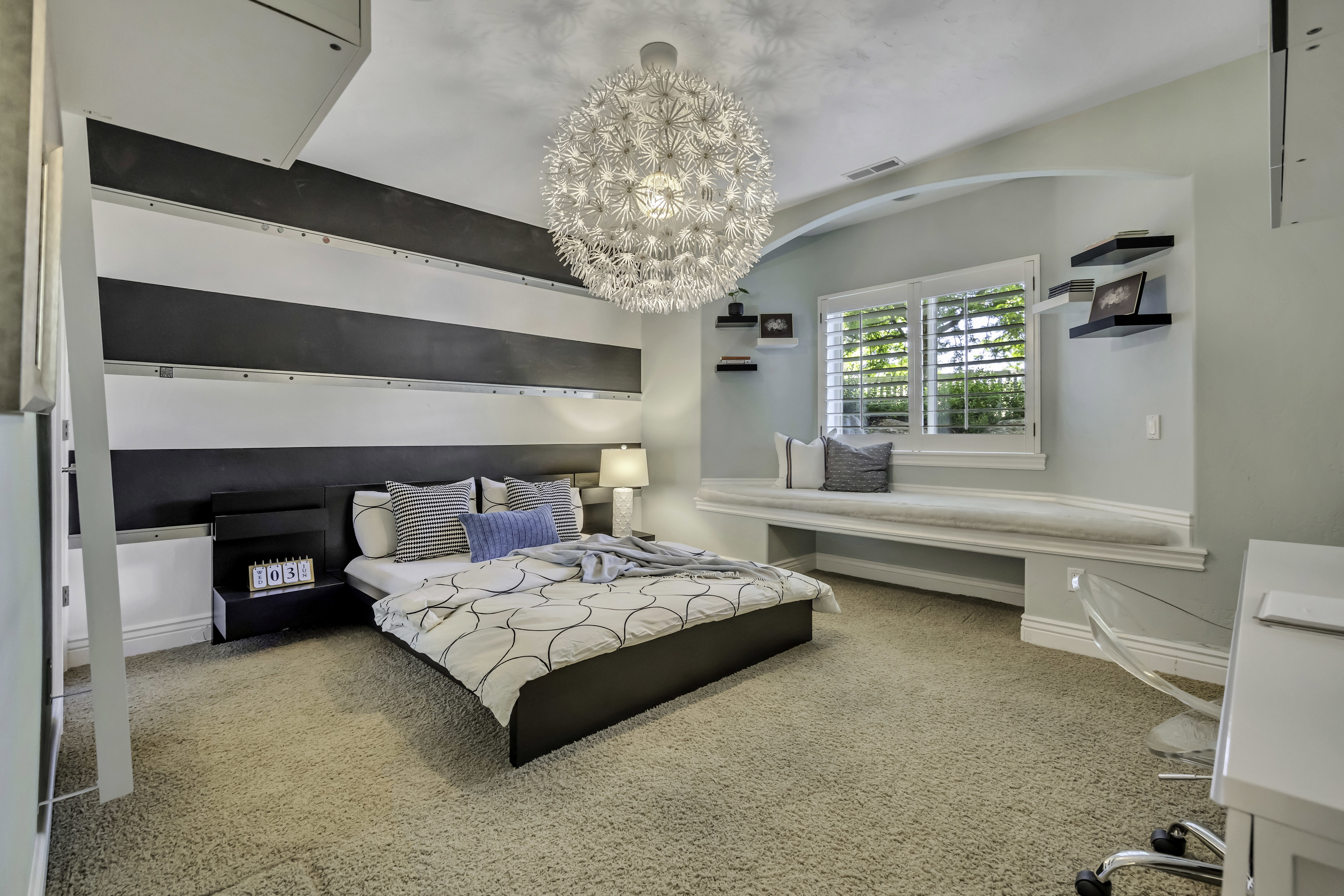 Carpeted room featuring a built-in window seat with a white cushion, a striped accent wall with a built-in headboard, and a unique spherical ceiling light fixture
