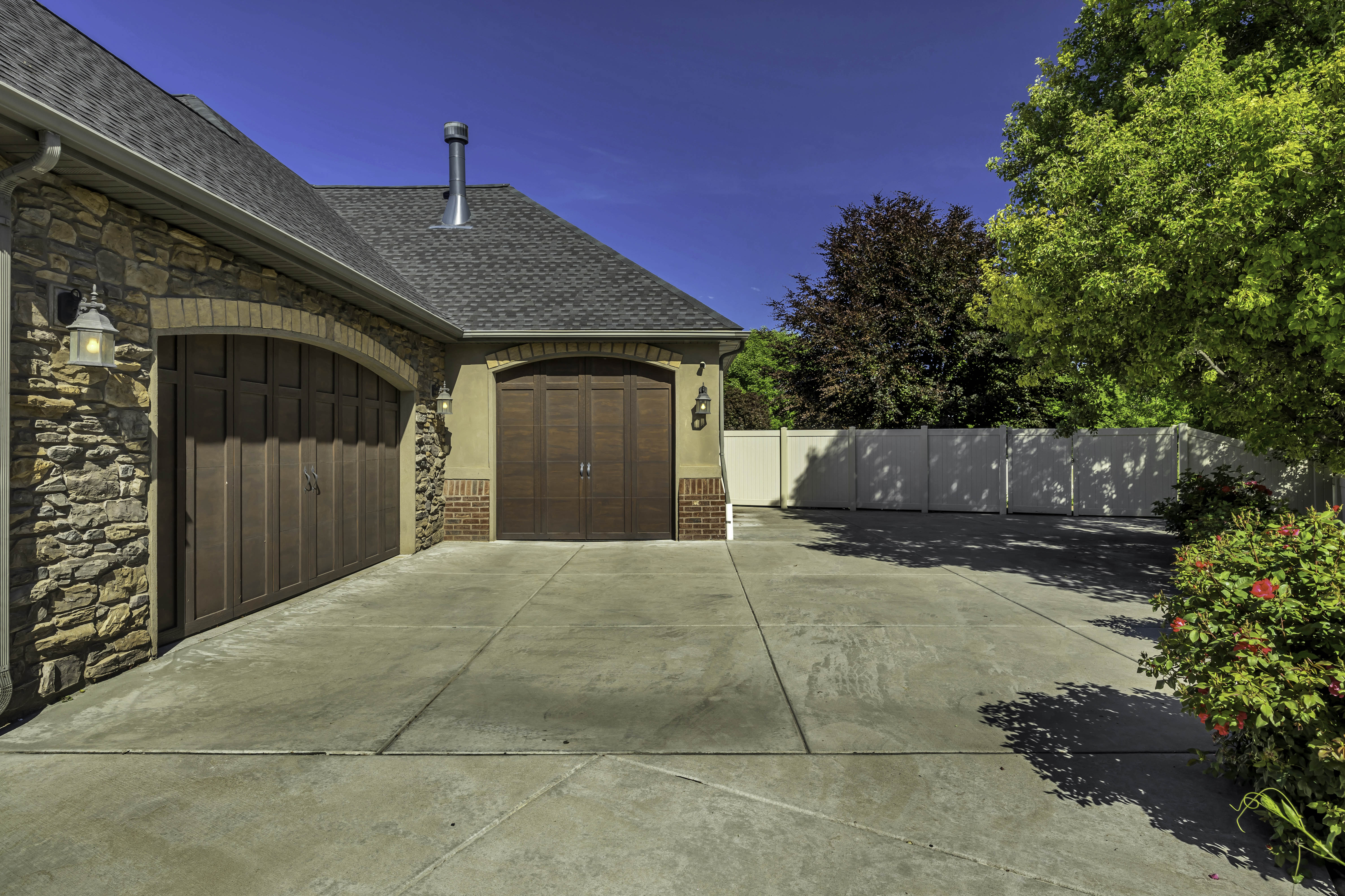 Spacious concrete driveway featuring two wood-panel garage doors with arched brick surrounds