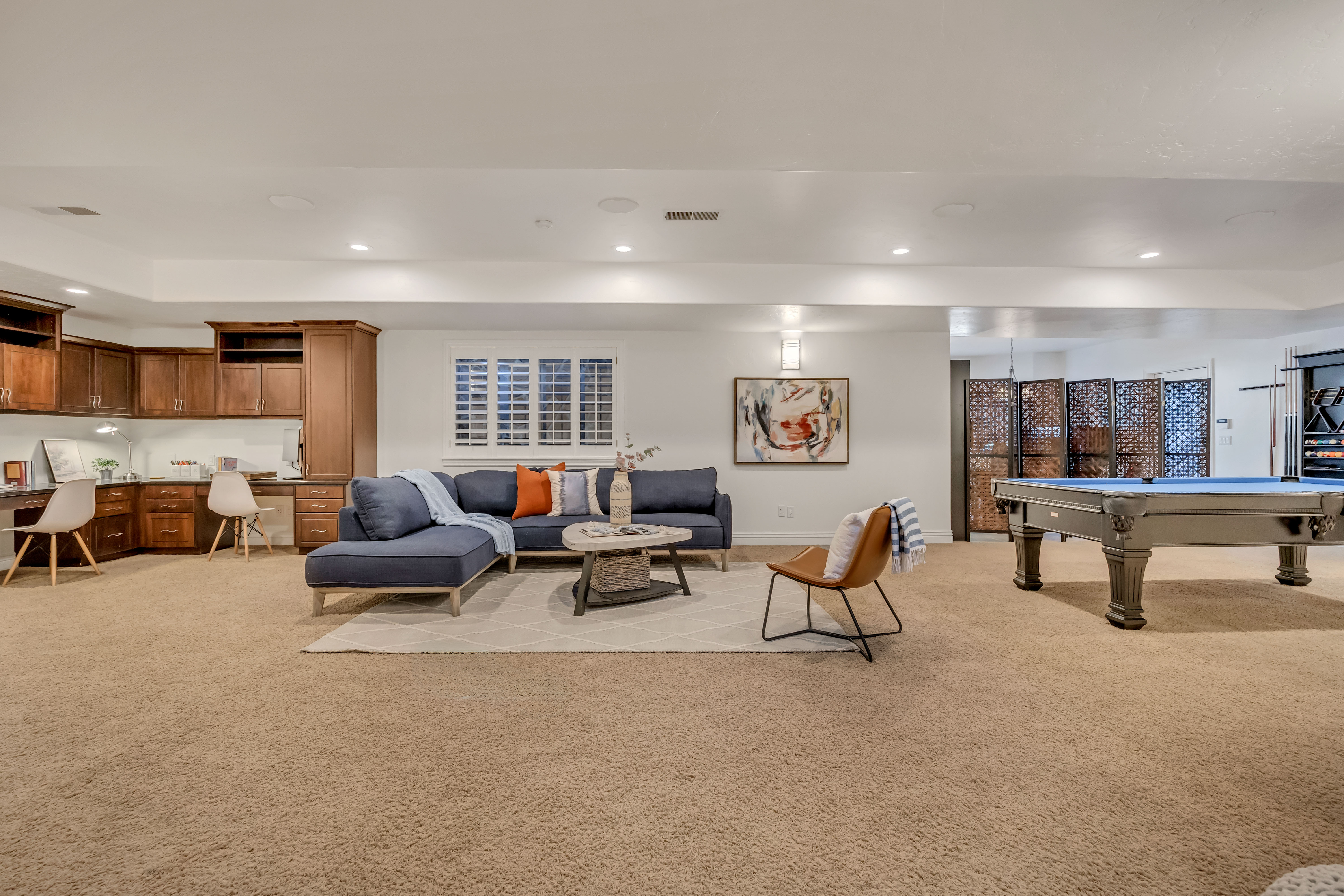 Spacious recreational room featuring a built-in cabinetry desk area, a window with plantation shutters, recessed lighting, and carpet flooring