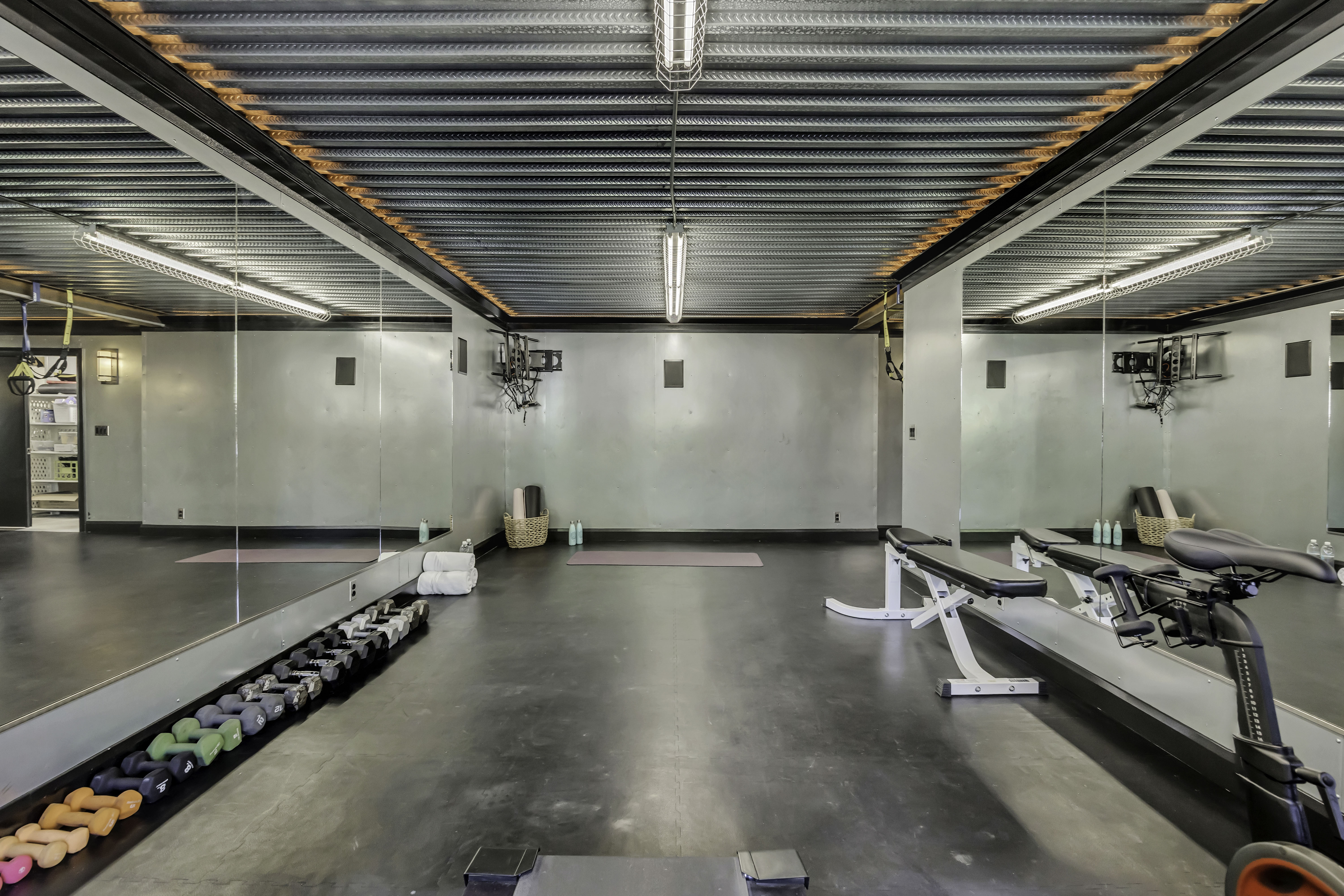 Spacious room featuring floor-to-ceiling mirrors, a durable rubber floor, and exposed industrial-style ceiling with integrated lighting
