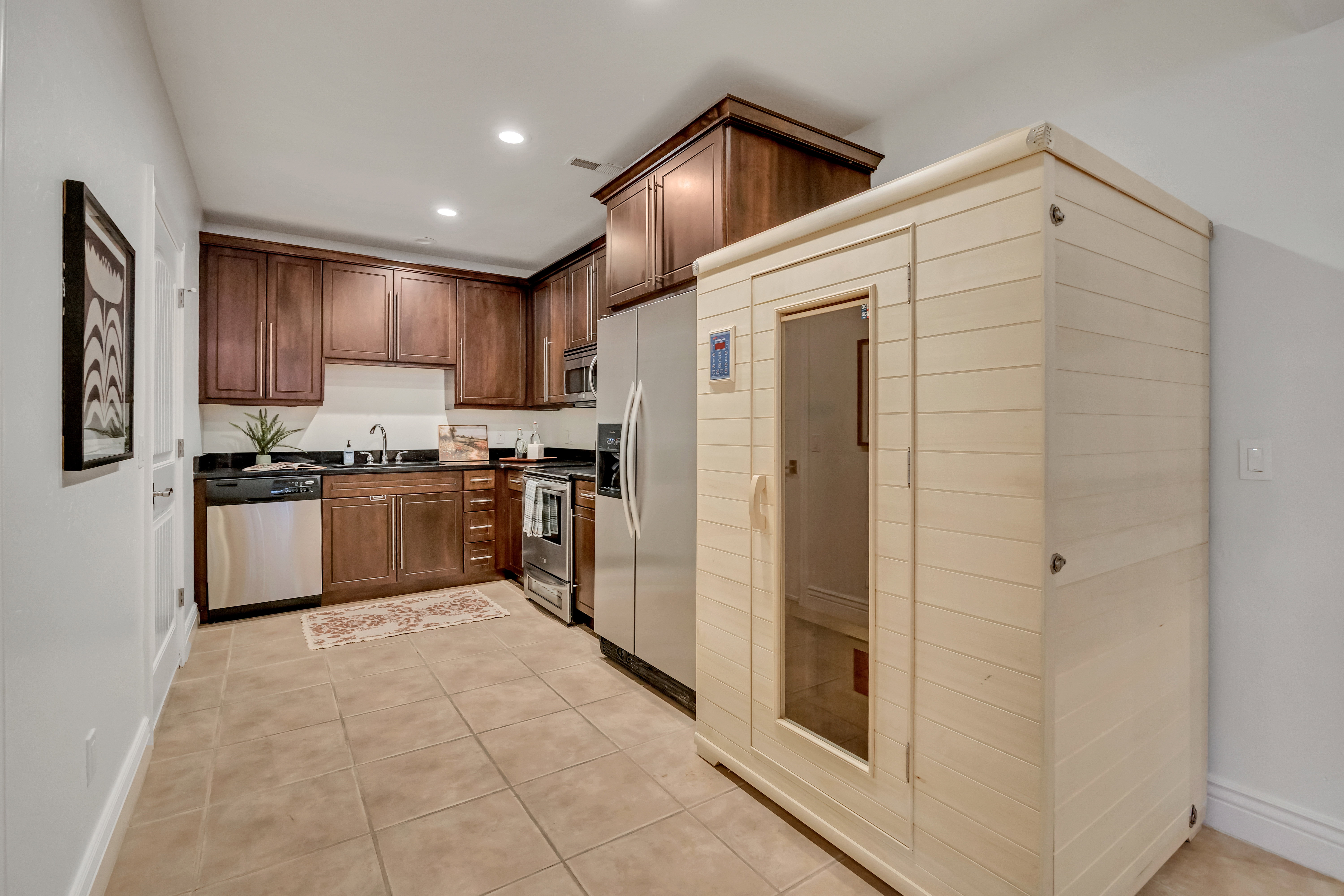 Kitchenette with wood cabinetry, dark countertops, and stainless steel appliances, featuring a built-in sauna unit