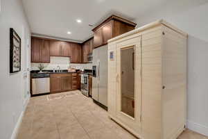 Kitchenette with wood cabinetry, dark countertops, and stainless steel appliances, featuring a built-in sauna unit