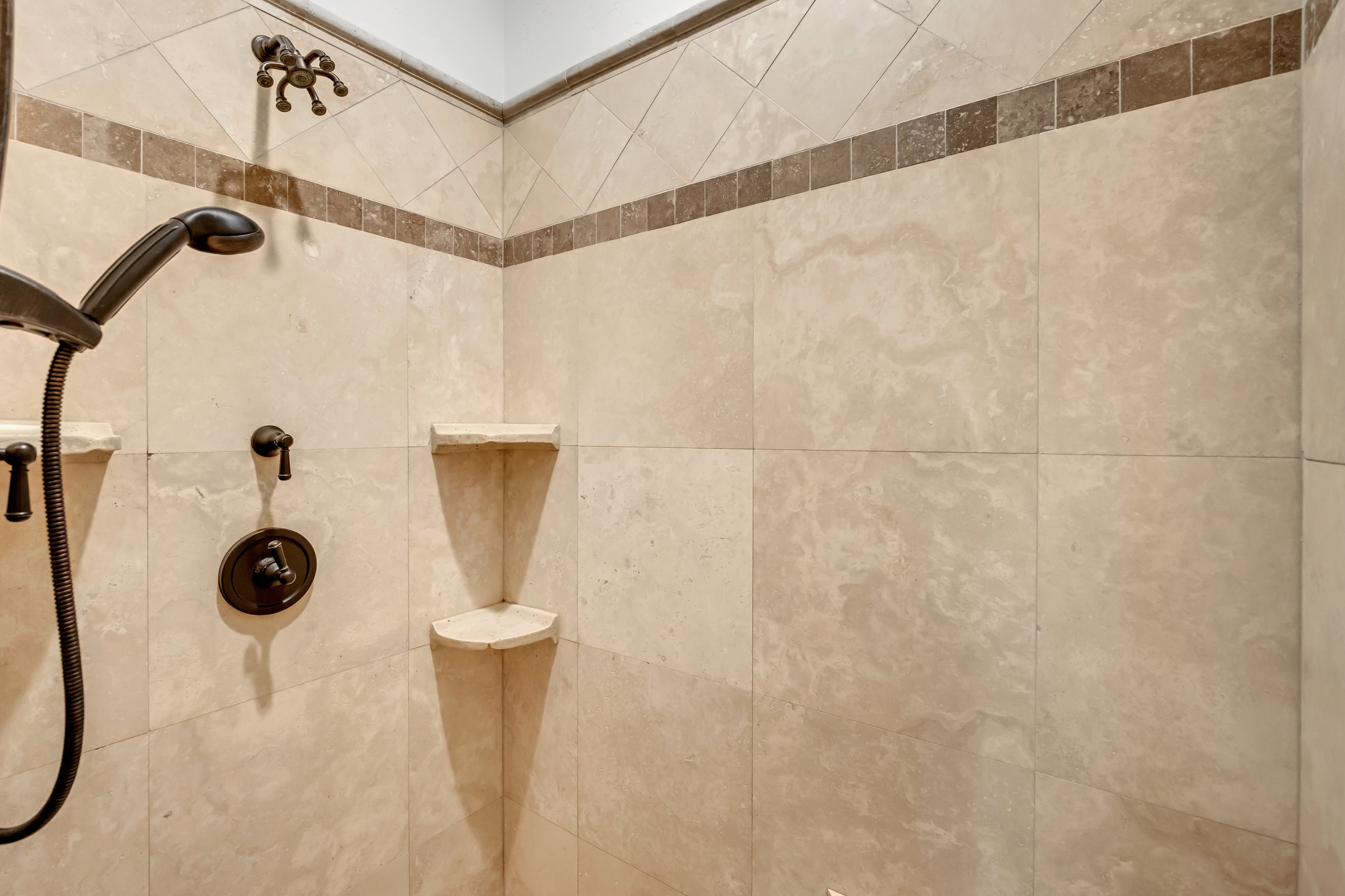Tiled shower enclosure featuring a handheld showerhead with bronze finish fixtures