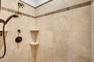 Tiled shower enclosure featuring a handheld showerhead with bronze finish fixtures