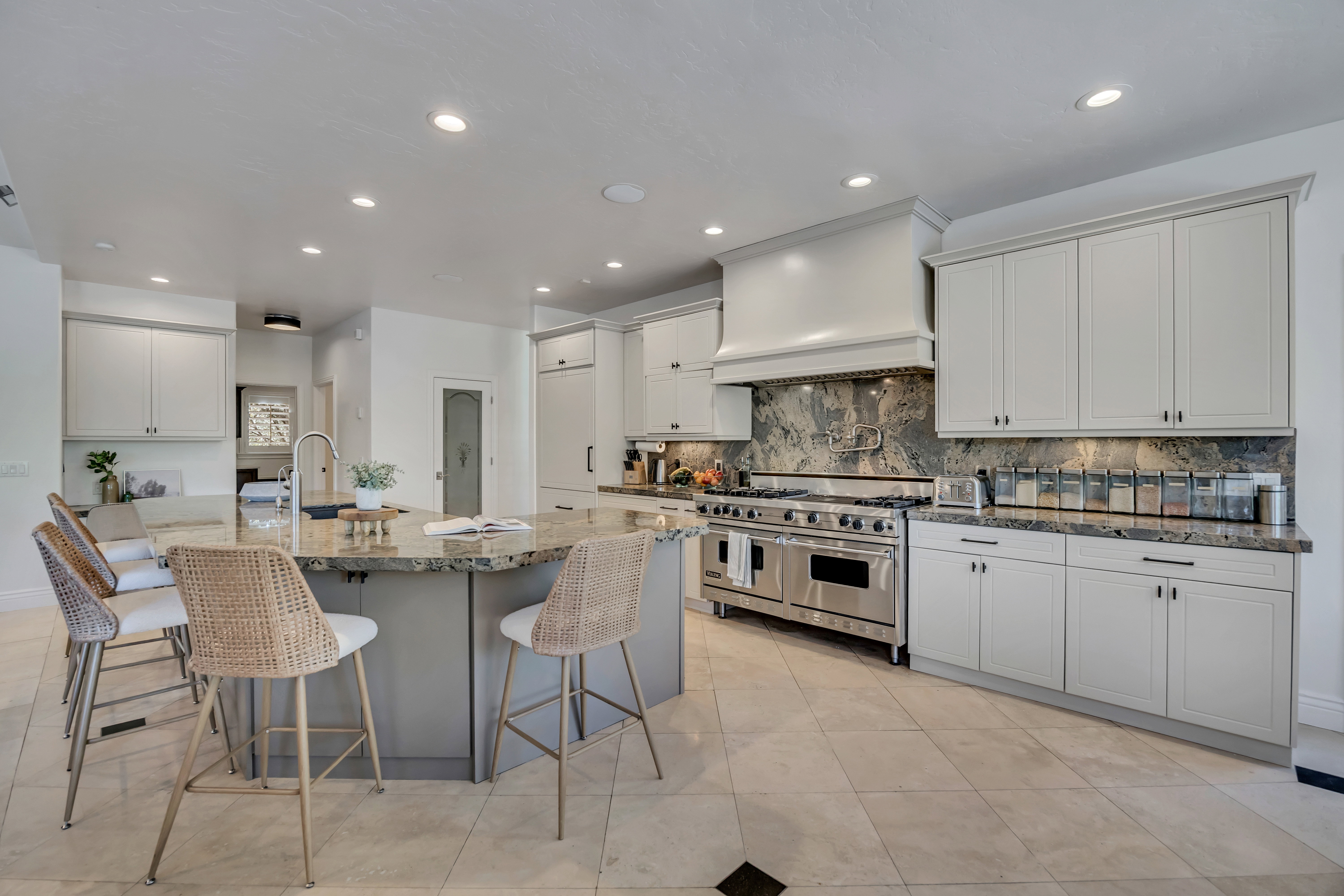 Kitchen featuring a substantial central island with integrated sink, stainless steel range with custom vent hood, light-toned cabinetry, natural stone countertops, and tile flooring