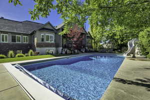 Expansive swimming pool with integrated slide, surrounded by concrete decking and mature trees