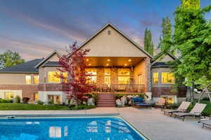 Rear exterior featuring a large in-ground swimming pool with a surrounding concrete patio, a covered patio with recessed lighting, and a stone accent wall