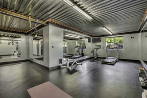 Dedicated fitness room featuring dark rubber flooring, mirrored walls, a corrugated metal ceiling with exposed beams, and fluorescent strip lighting