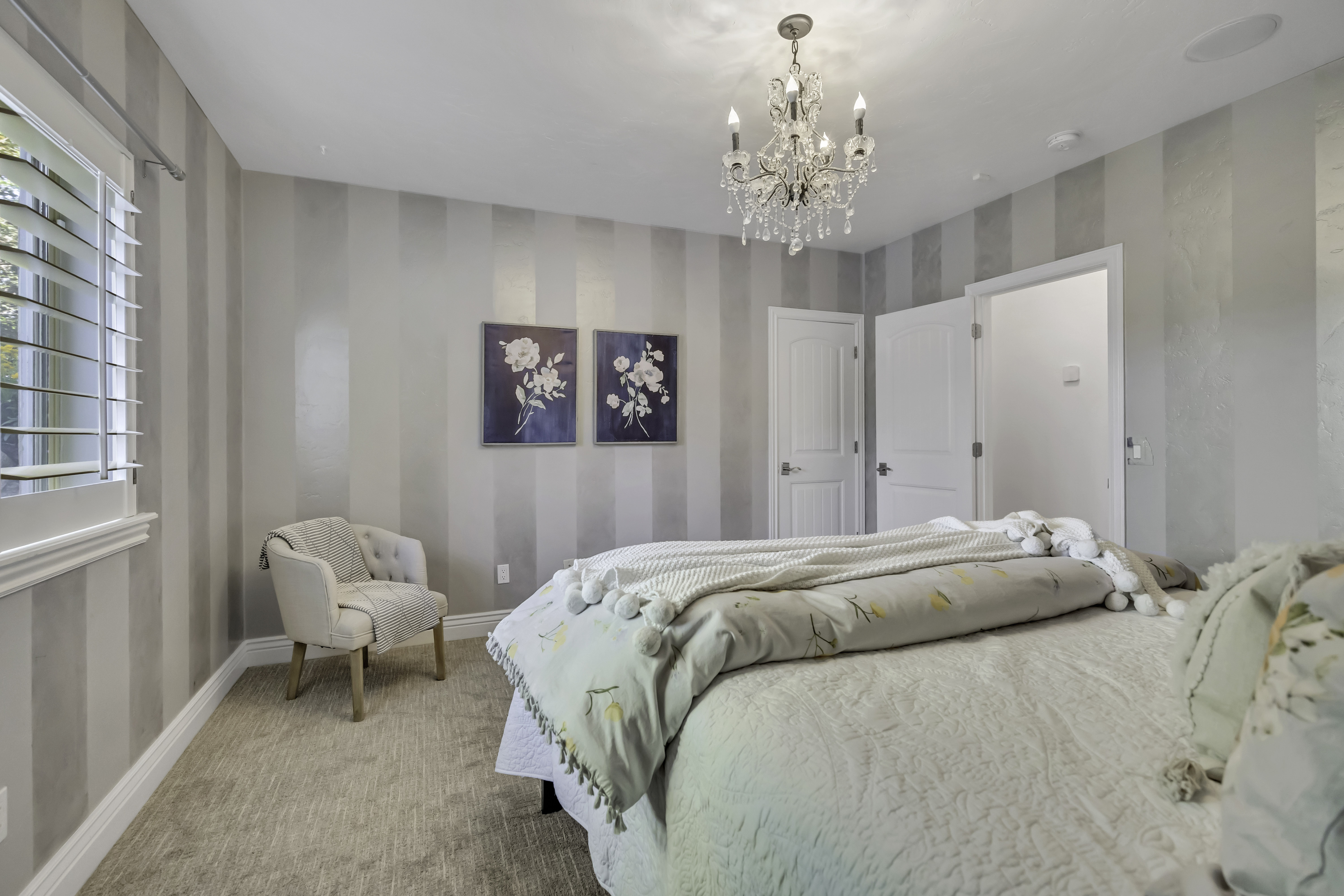 Bedroom featuring striped accent walls, plush carpet flooring, a crystal chandelier, and shuttered windows