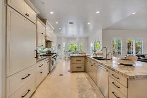 Gourmet kitchen featuring a large island with sink, stainless steel appliances, extensive cabinetry, stone countertops, and recessed lighting
