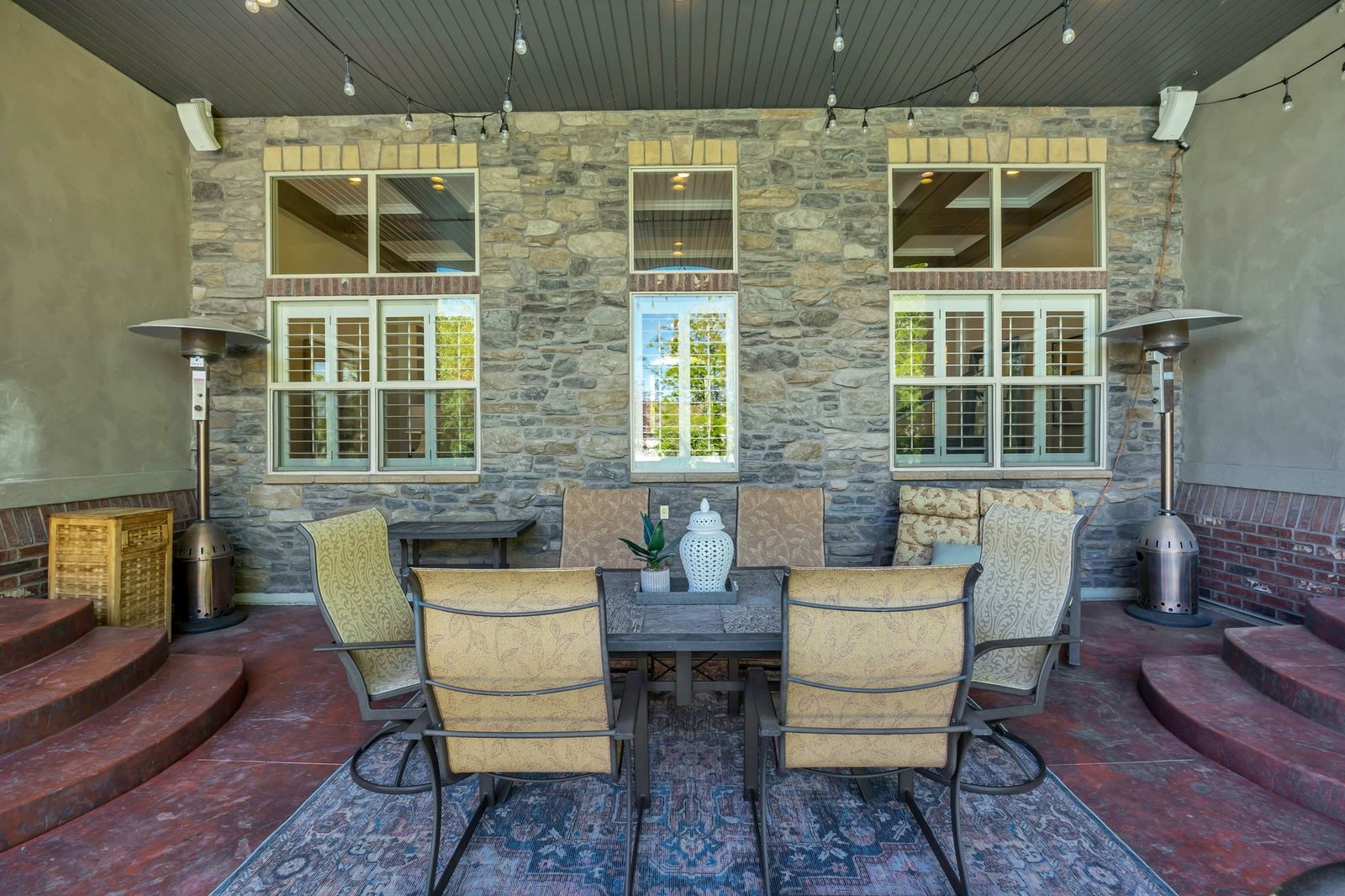 Covered patio featuring a stone veneer wall, shuttered windows, and a ceiling with integrated lighting