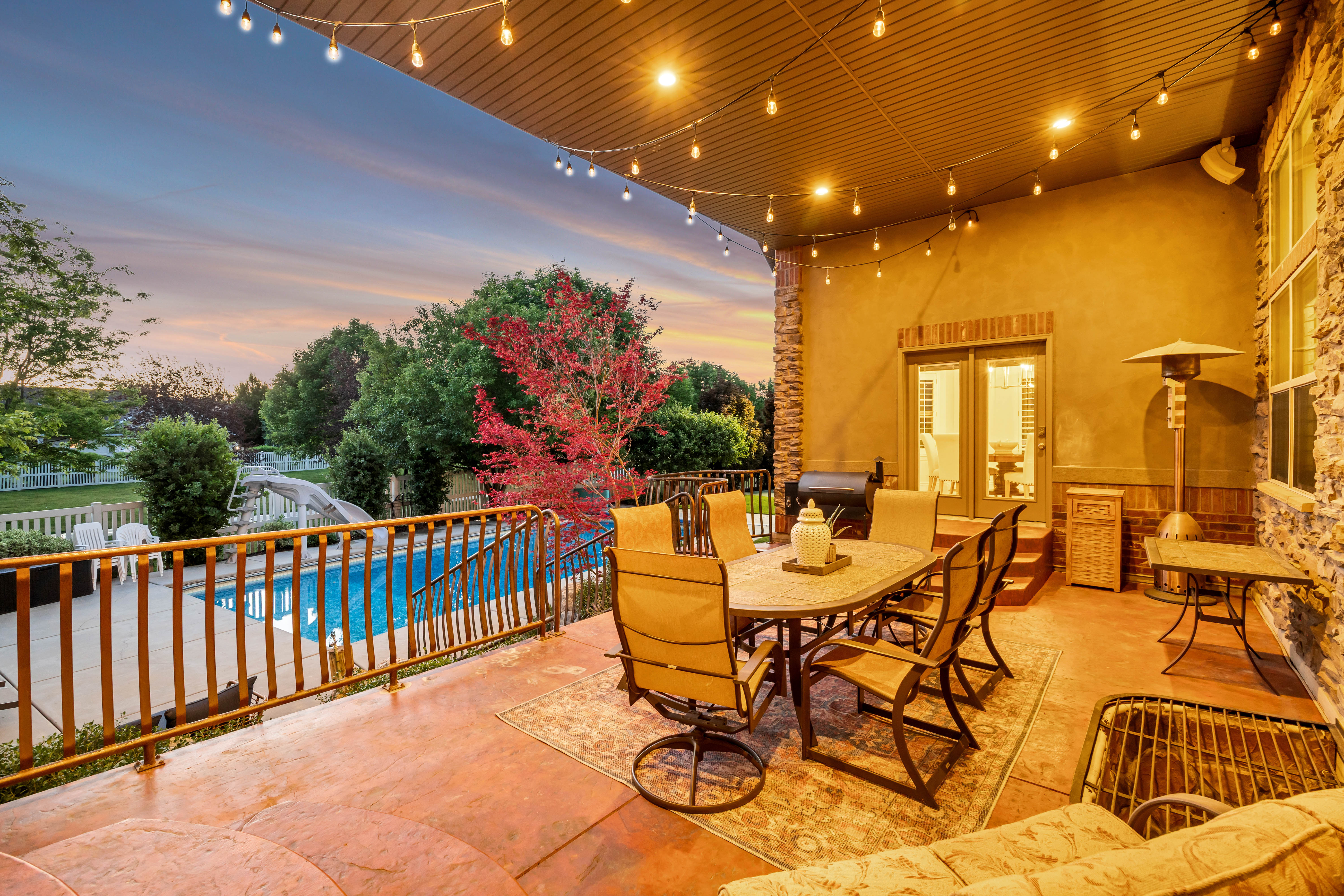 Covered patio with string lighting, direct access to the interior via French doors, and a stone-clad exterior wall