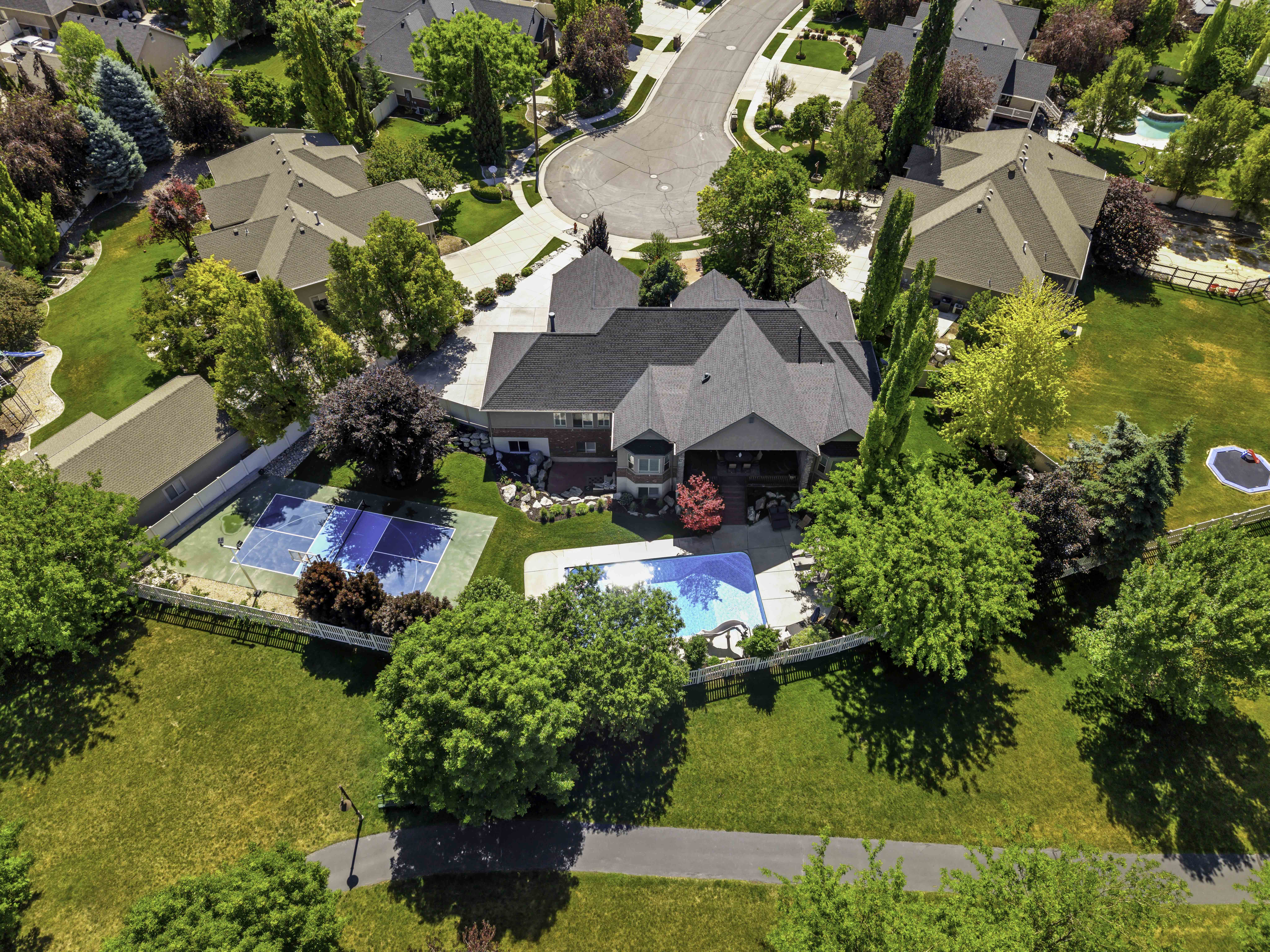 Expansive property featuring a large residence with a multi-gabled roof, an in-ground swimming pool, a dedicated sports court, a paved walking path, and mature landscaping