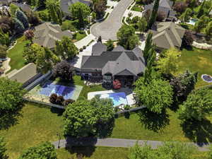 Expansive property featuring a large residence with a multi-gabled roof, an in-ground swimming pool, a dedicated sports court, a paved walking path, and mature landscaping