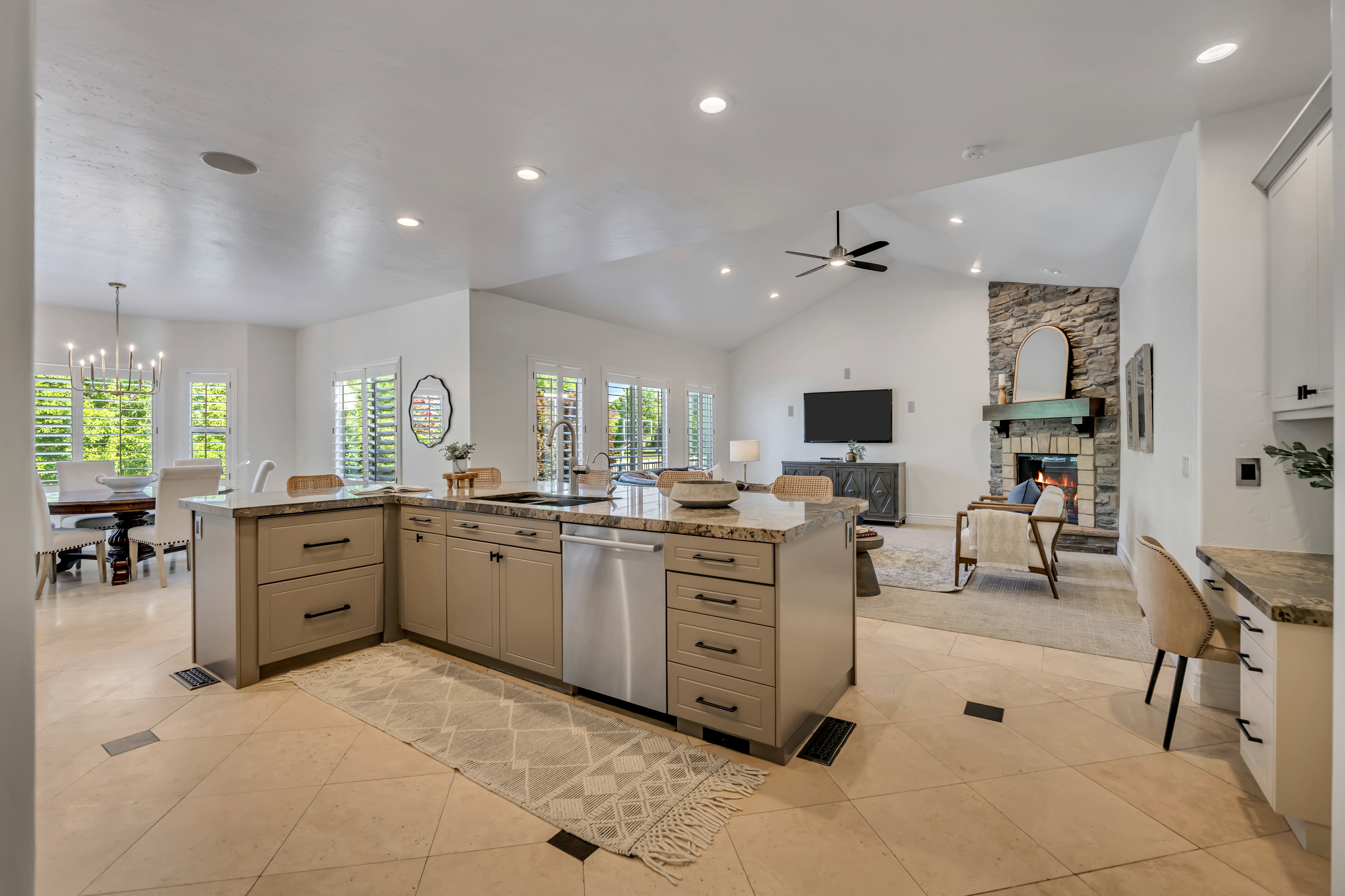 Open-concept living space featuring a kitchen island with stone countertops and integrated sink, stainless steel dishwasher, vaulted ceiling with recessed lighting, and a stone fireplace with a wood mantel