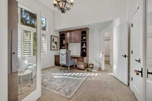 Dedicated office space featuring built-in wood cabinetry with shelving, high ceilings, and an ornate chandelier