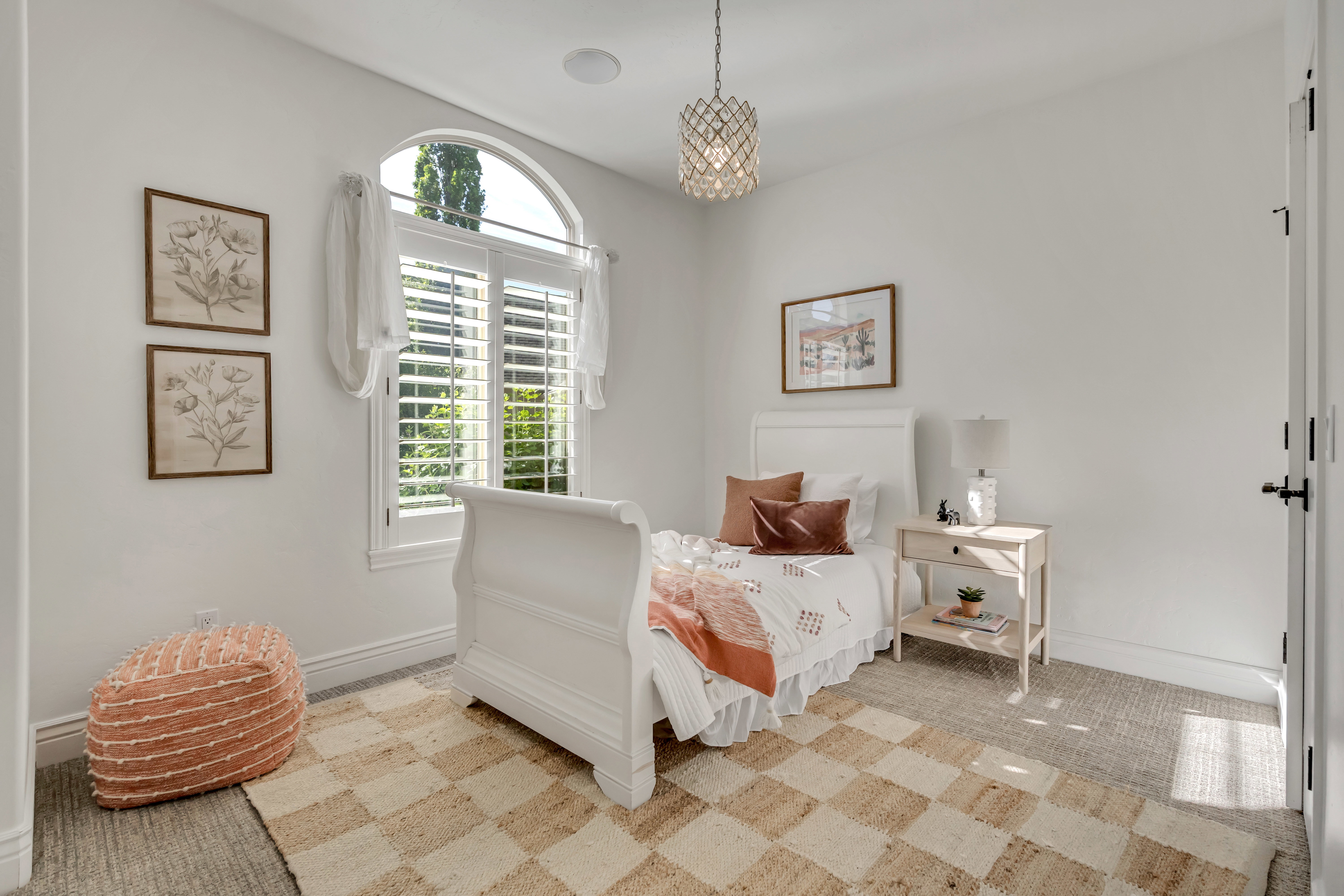 Bright room featuring an arched window with plantation shutters, a decorative chandelier, and light-toned walls