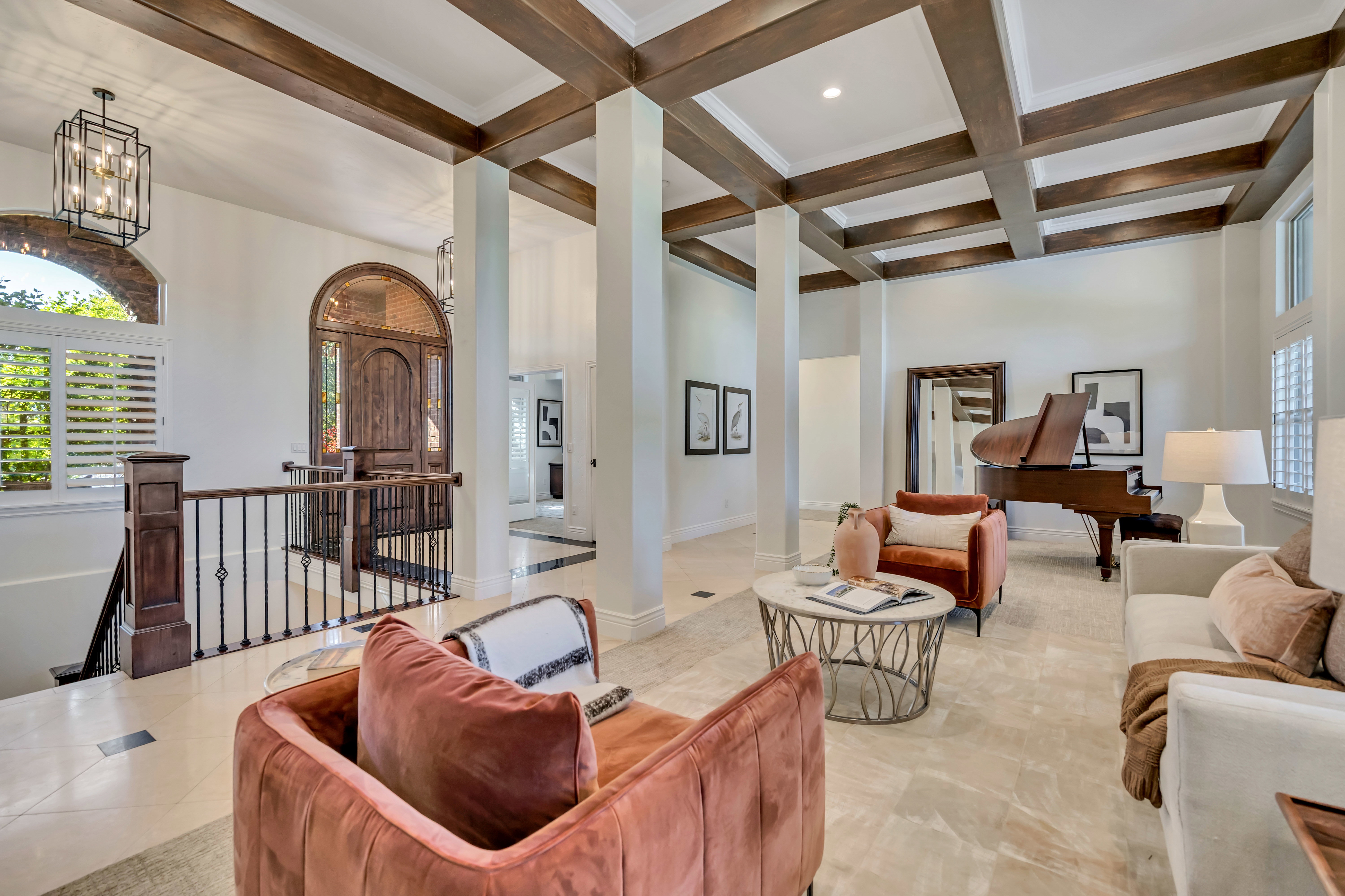 Formal living area featuring a coffered ceiling with exposed wood beams, light-toned tile flooring, and a grand arched entry door with custom wood detailing