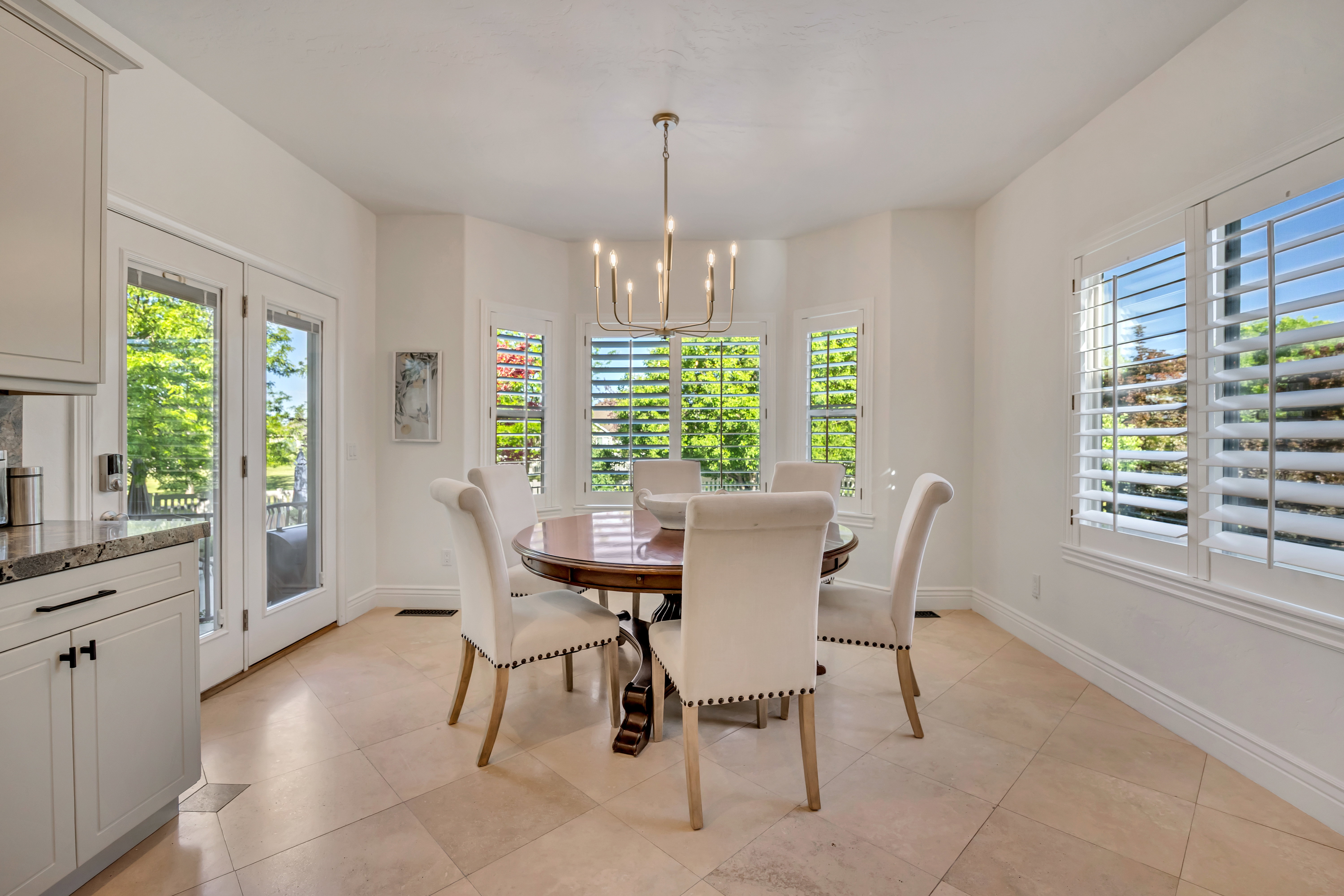 Dining area featuring tiled flooring, a bay window with plantation shutters, French doors, and a chandelier