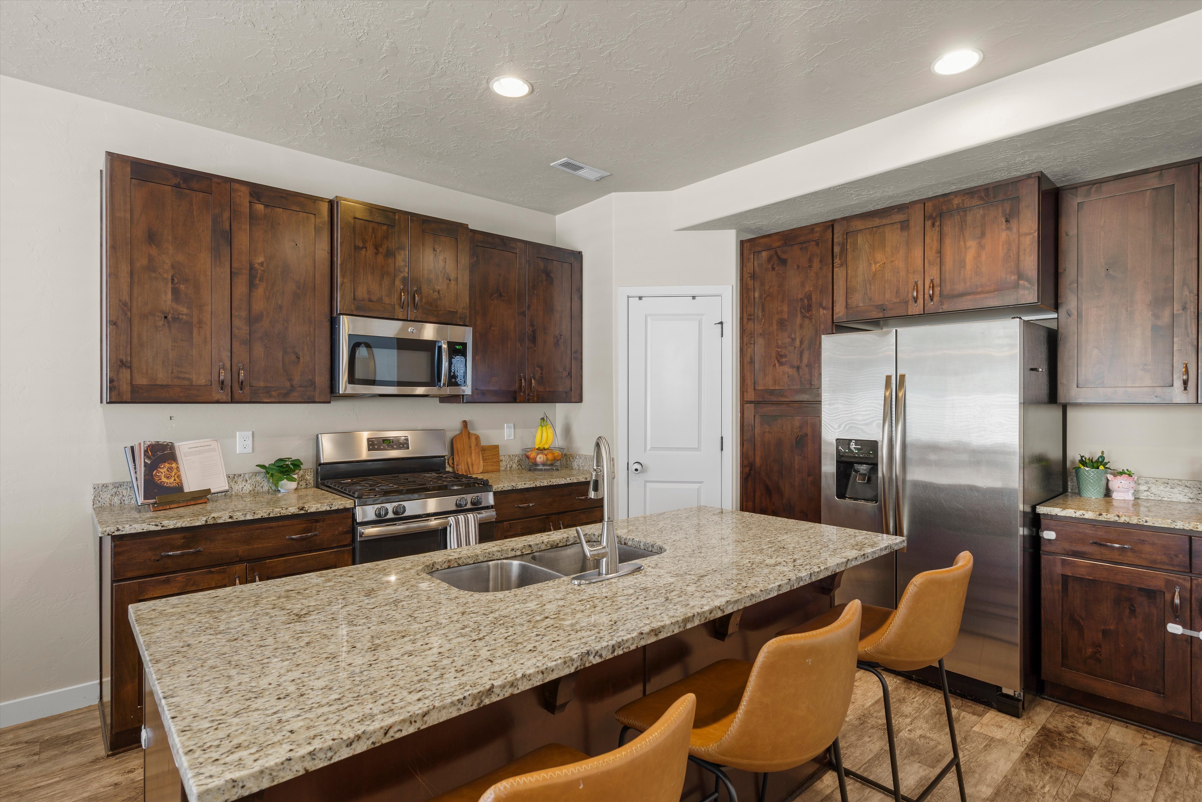 Kitchen featuring a large island with an undermount double sink, granite countertops, wood-finish cabinetry, stainless steel appliances, and recessed lighting