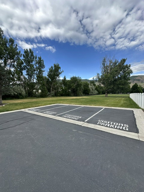 Paved parking area with designated visitor spaces, bordered by a concrete curb and an expanse of green lawn