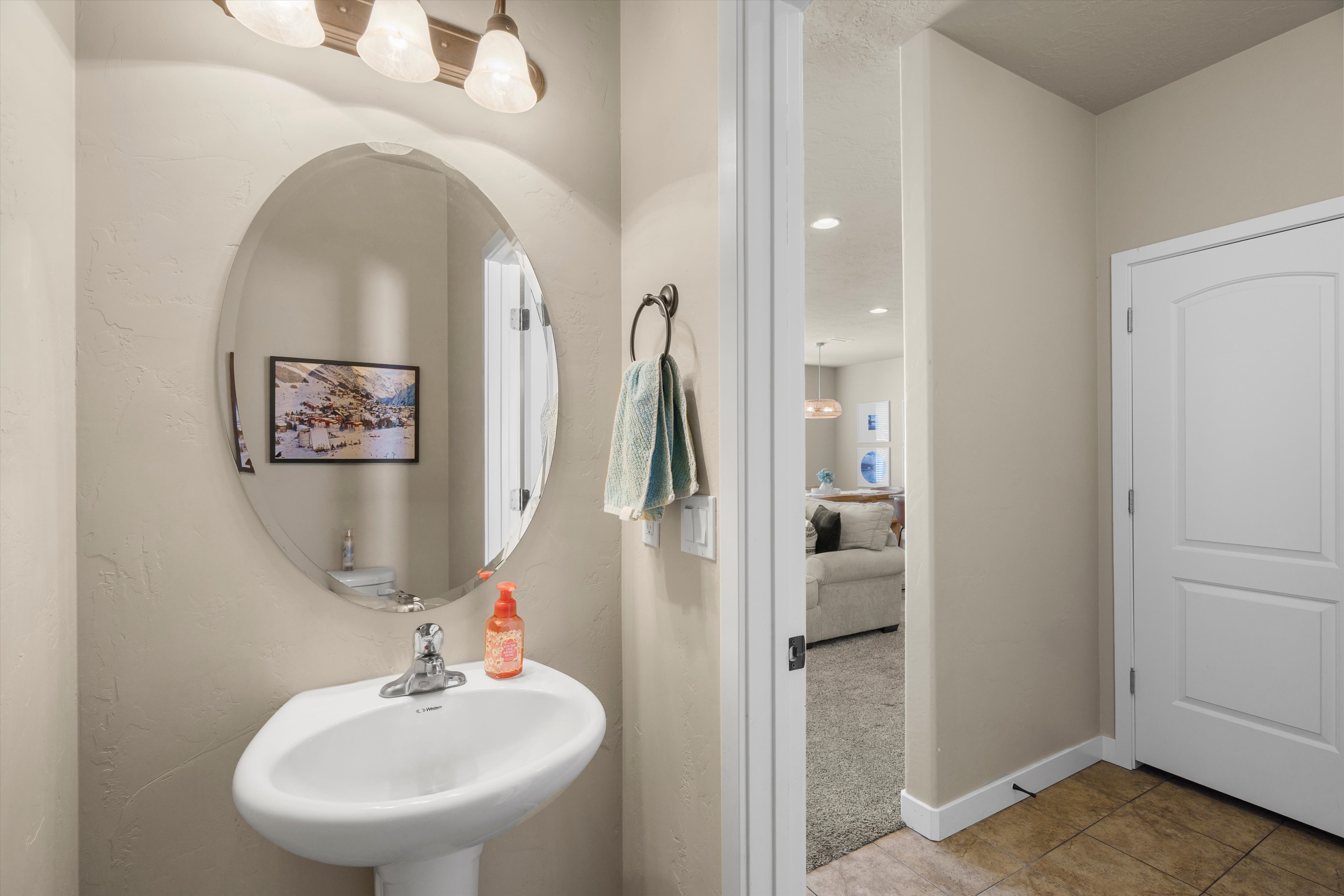 Pedestal sink with a chrome faucet, illuminated by a three-light vanity fixture