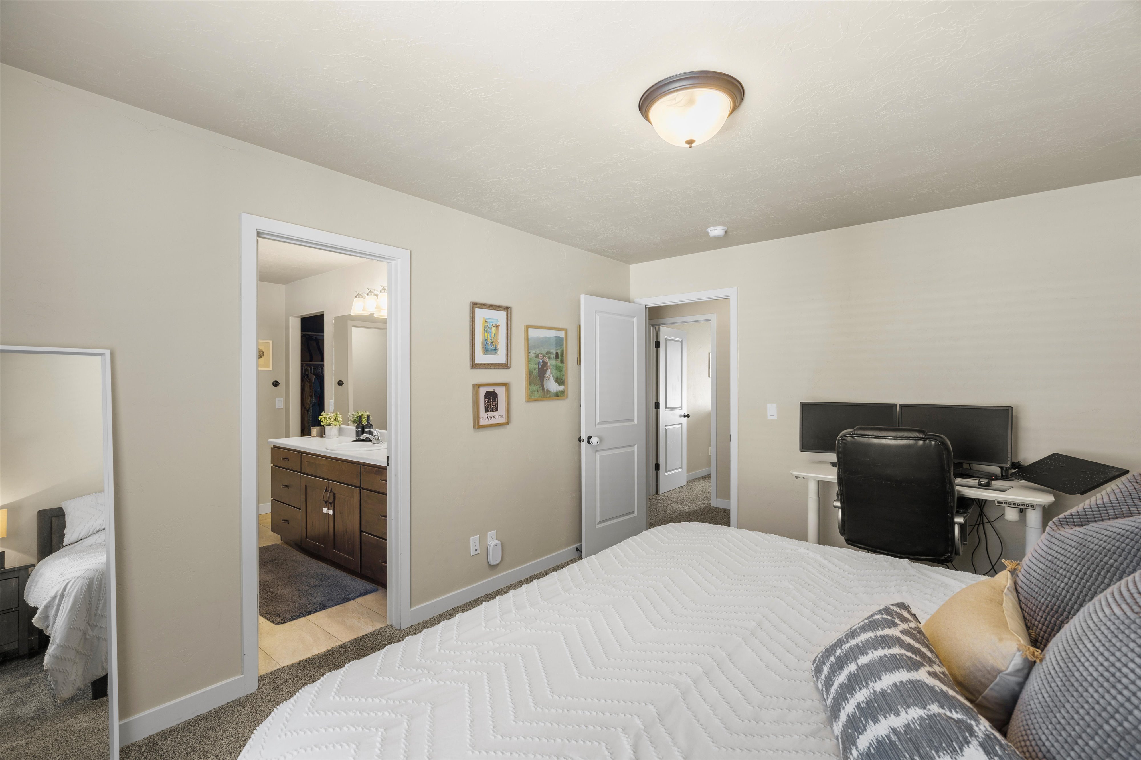 Bedroom featuring neutral wall color, carpet flooring, a ceiling-mounted light fixture, and an open doorway to a bathroom with a wood-finish vanity and white countertop