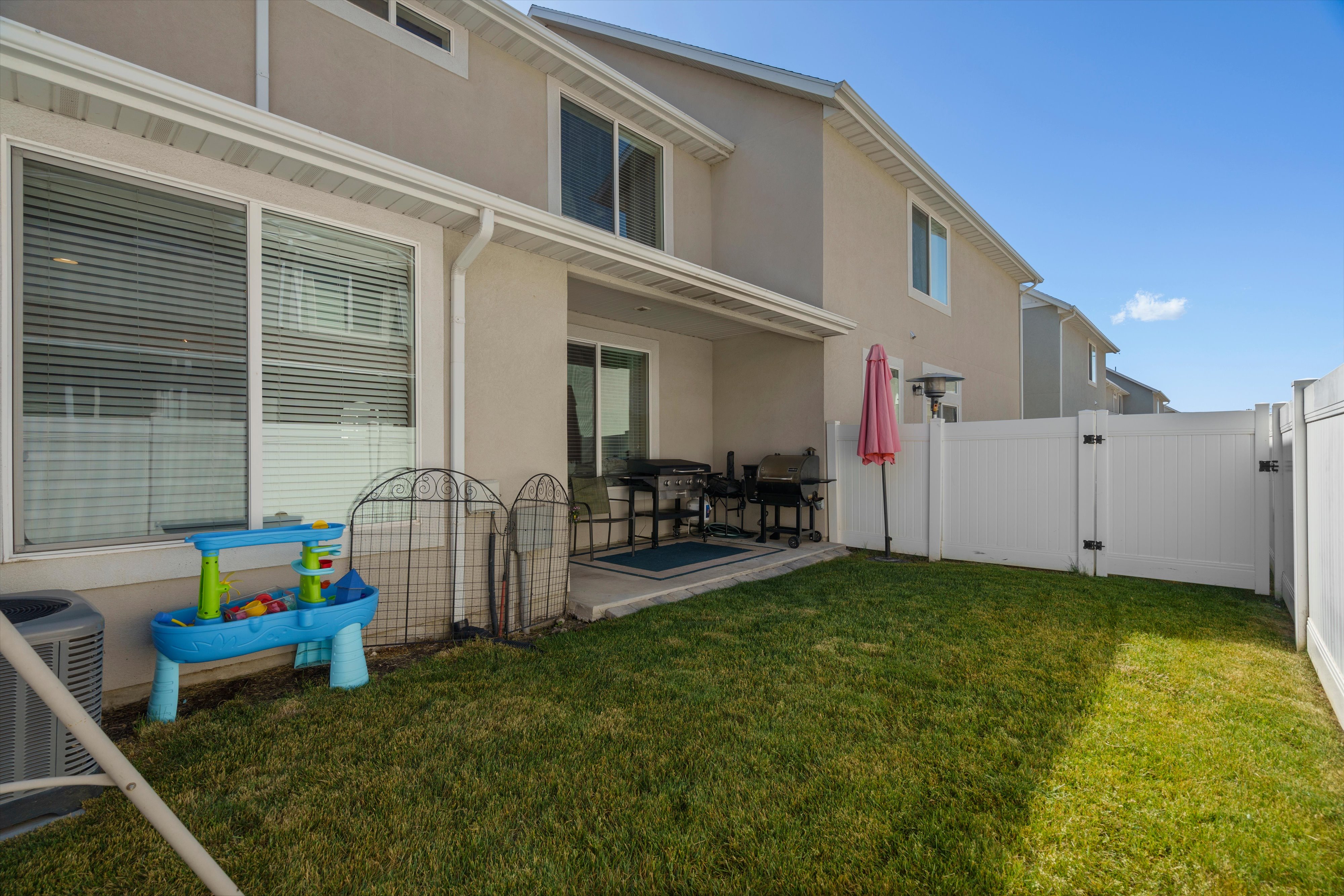 Expansive fenced backyard featuring a manicured lawn, a covered patio area, and a white privacy fence