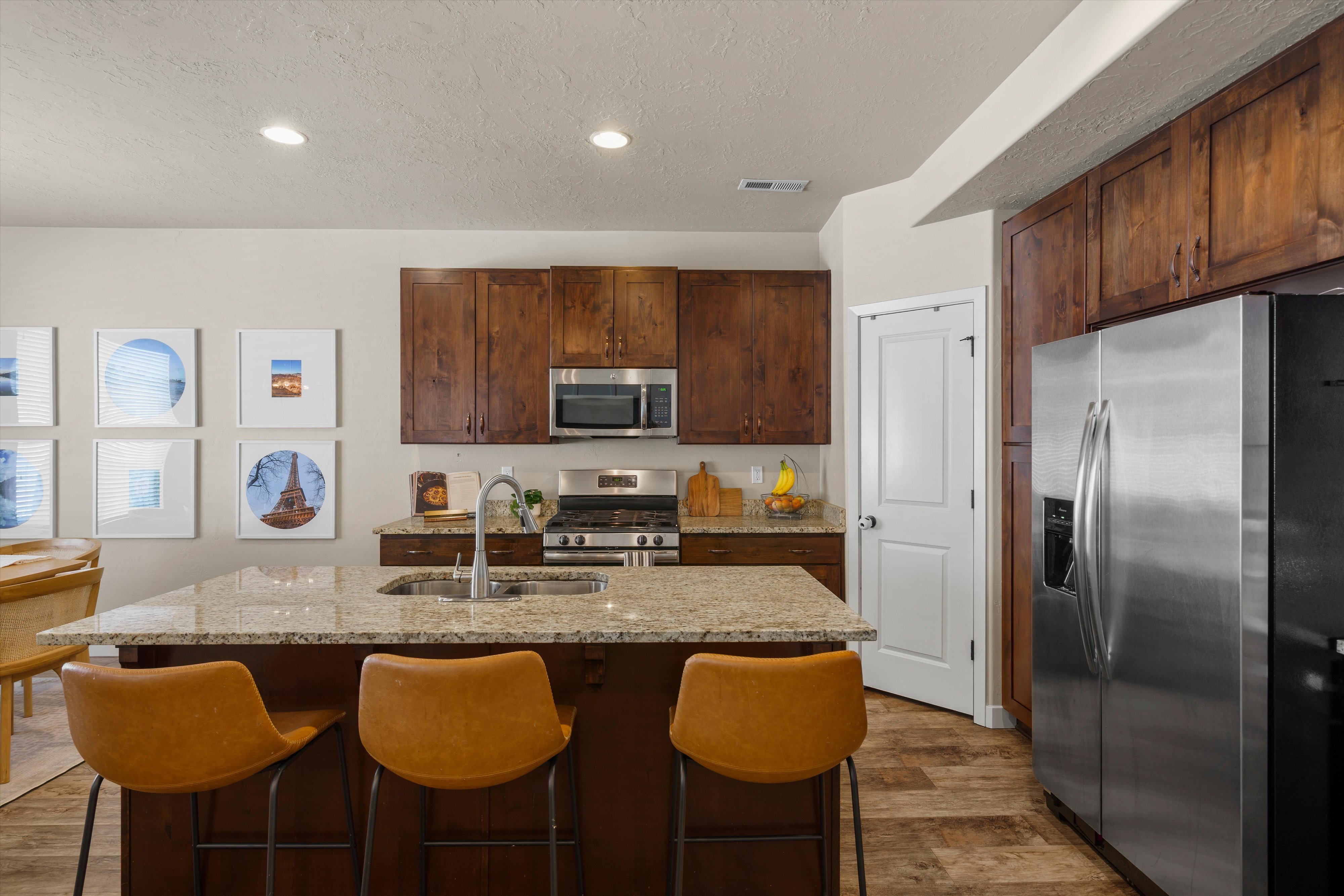 Kitchen featuring a large island with an undermount sink, granite countertops, wood-finish cabinetry, stainless steel appliances, and recessed lighting
