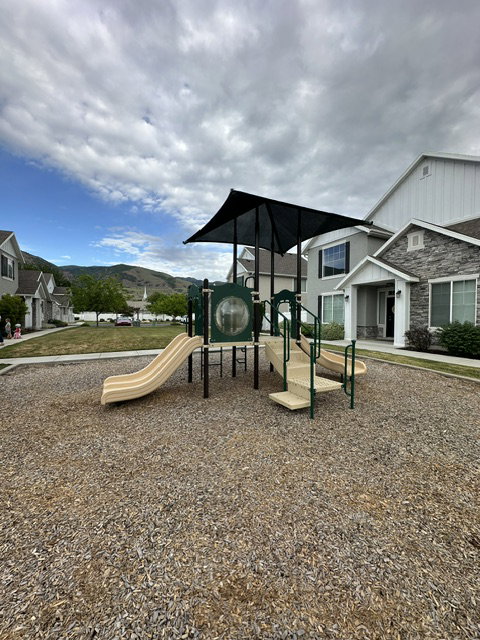 Community playground featuring multiple slides, stairs, a covered play structure, and woodchip ground cover