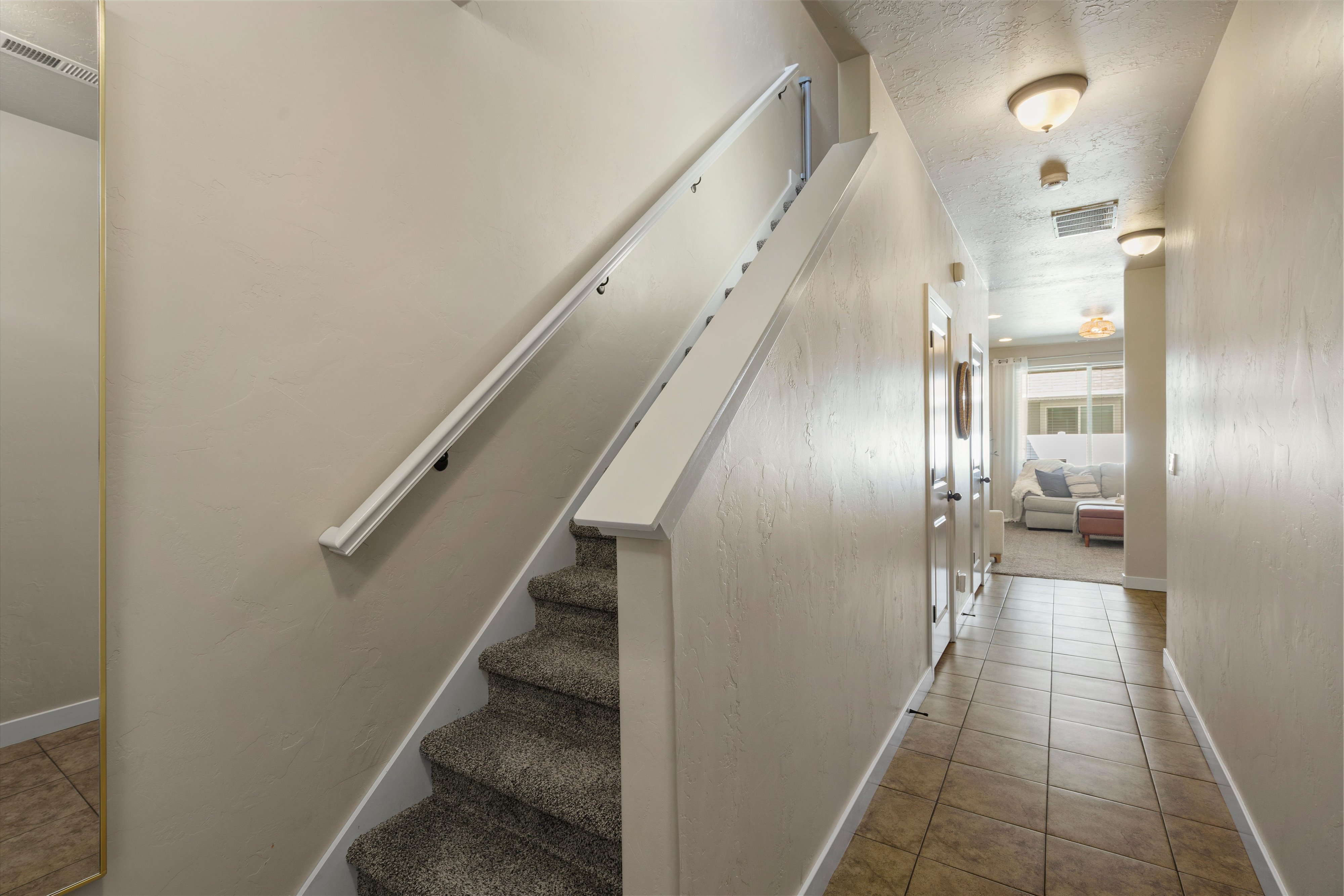 Hallway with tile flooring, featuring a carpeted staircase with white handrails and trim