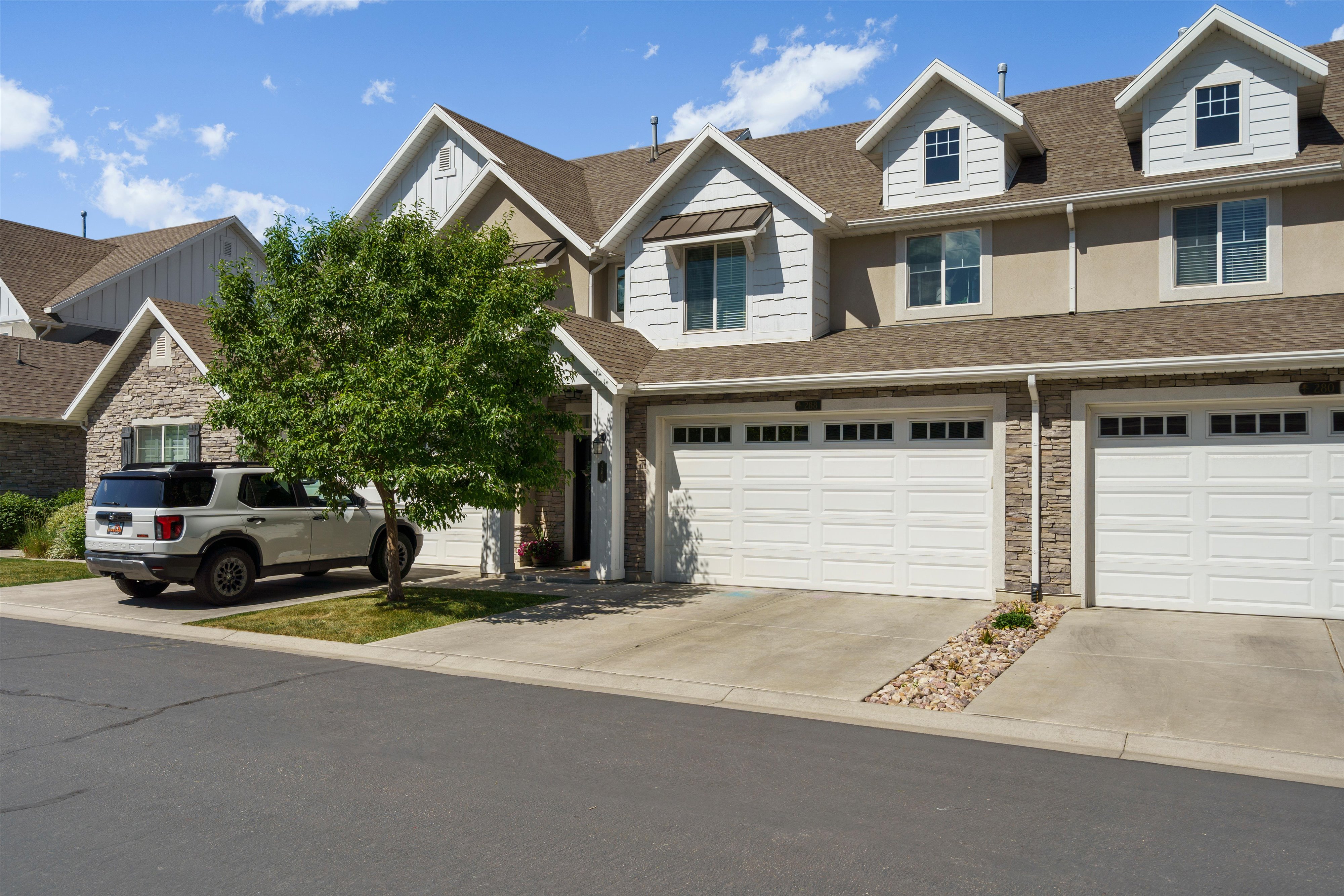 Townhome exterior featuring a two-car garage with paneling, stone facade accents, and dormer windows