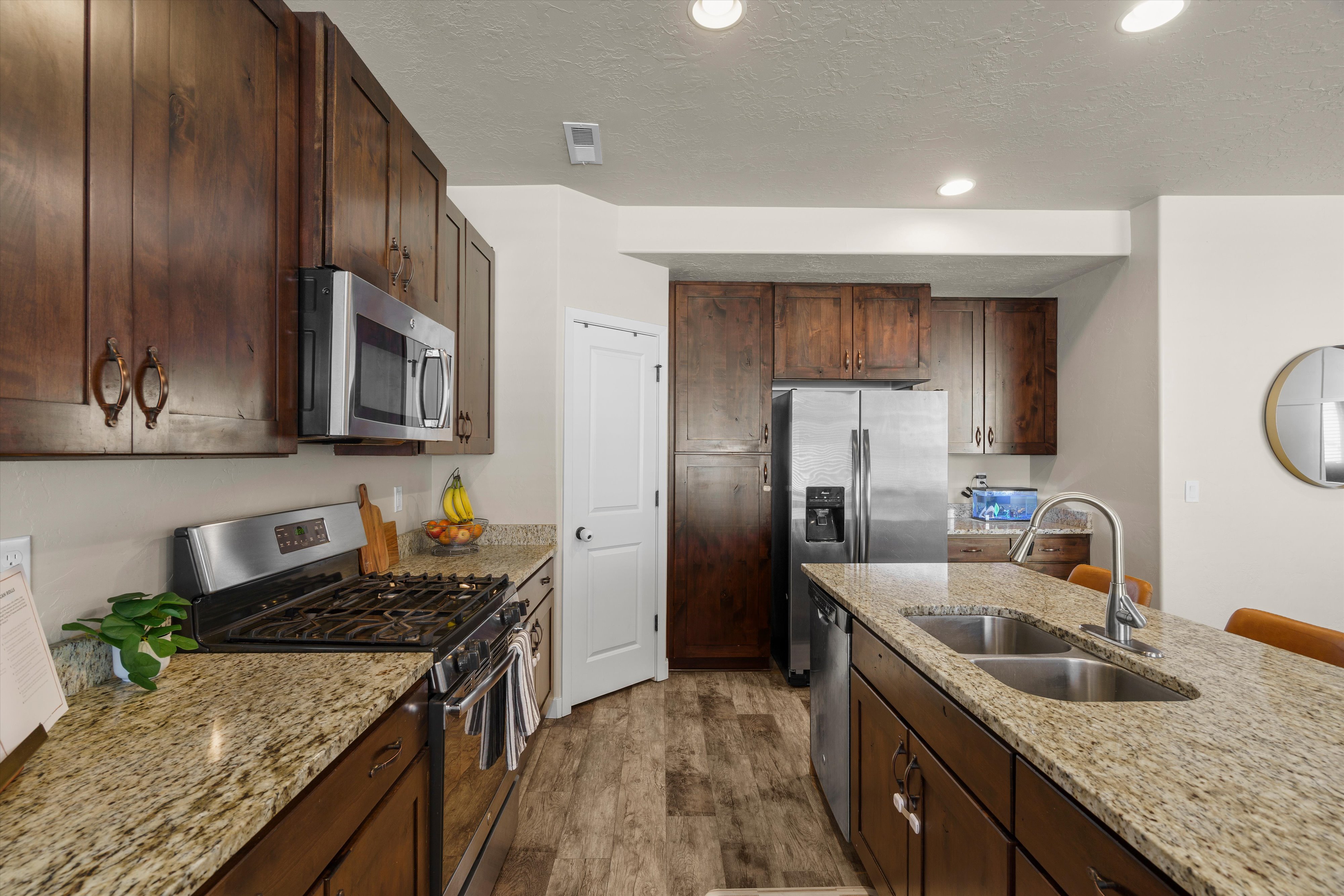 Gourmet kitchen featuring rich wood cabinetry, granite countertops, stainless steel appliances, a gas range, and a double basin kitchen island sink with a gooseneck faucet
