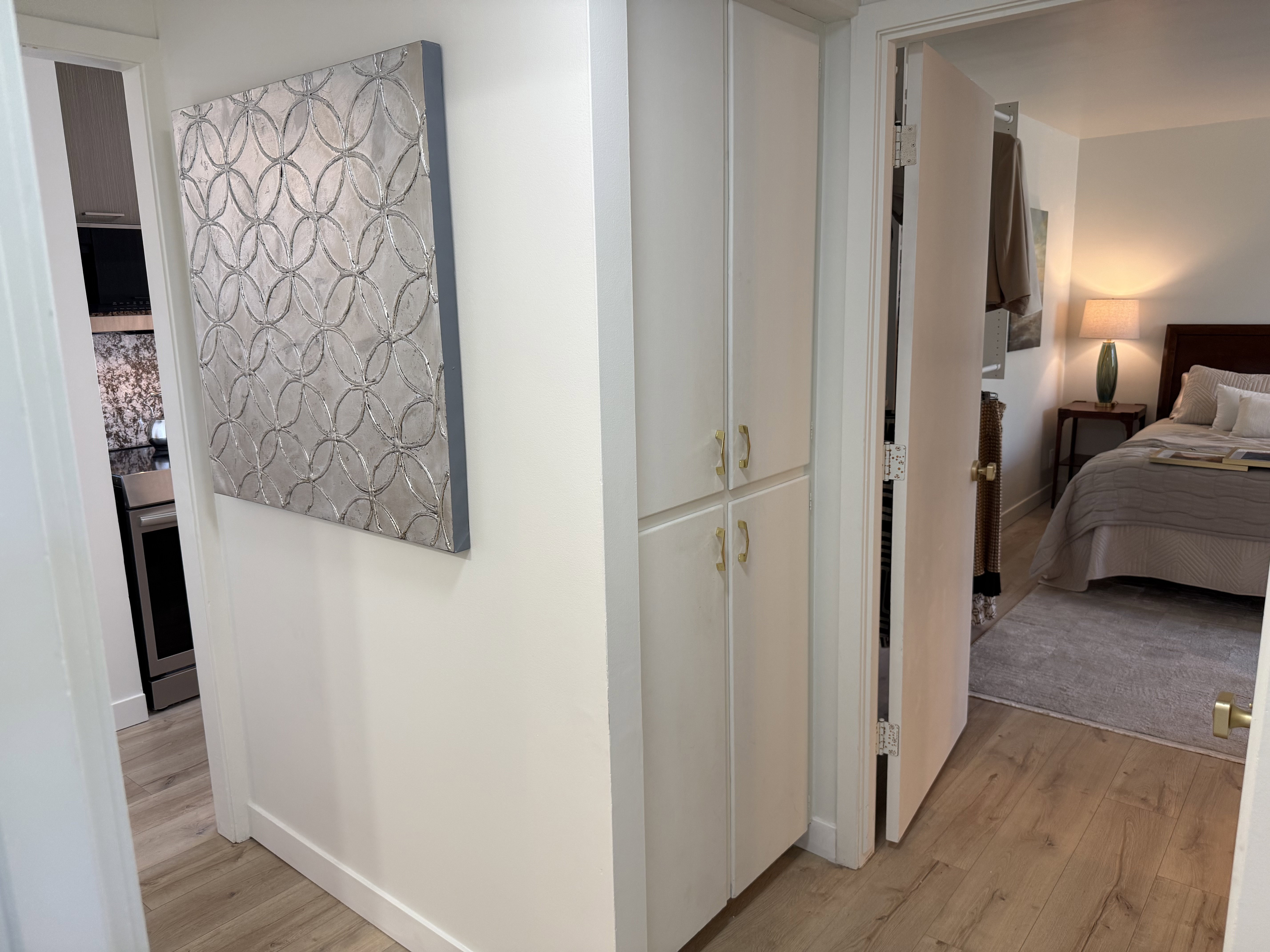 Hallway featuring wood-finish flooring, built-in white cabinetry with gold-tone hardware, and white baseboards