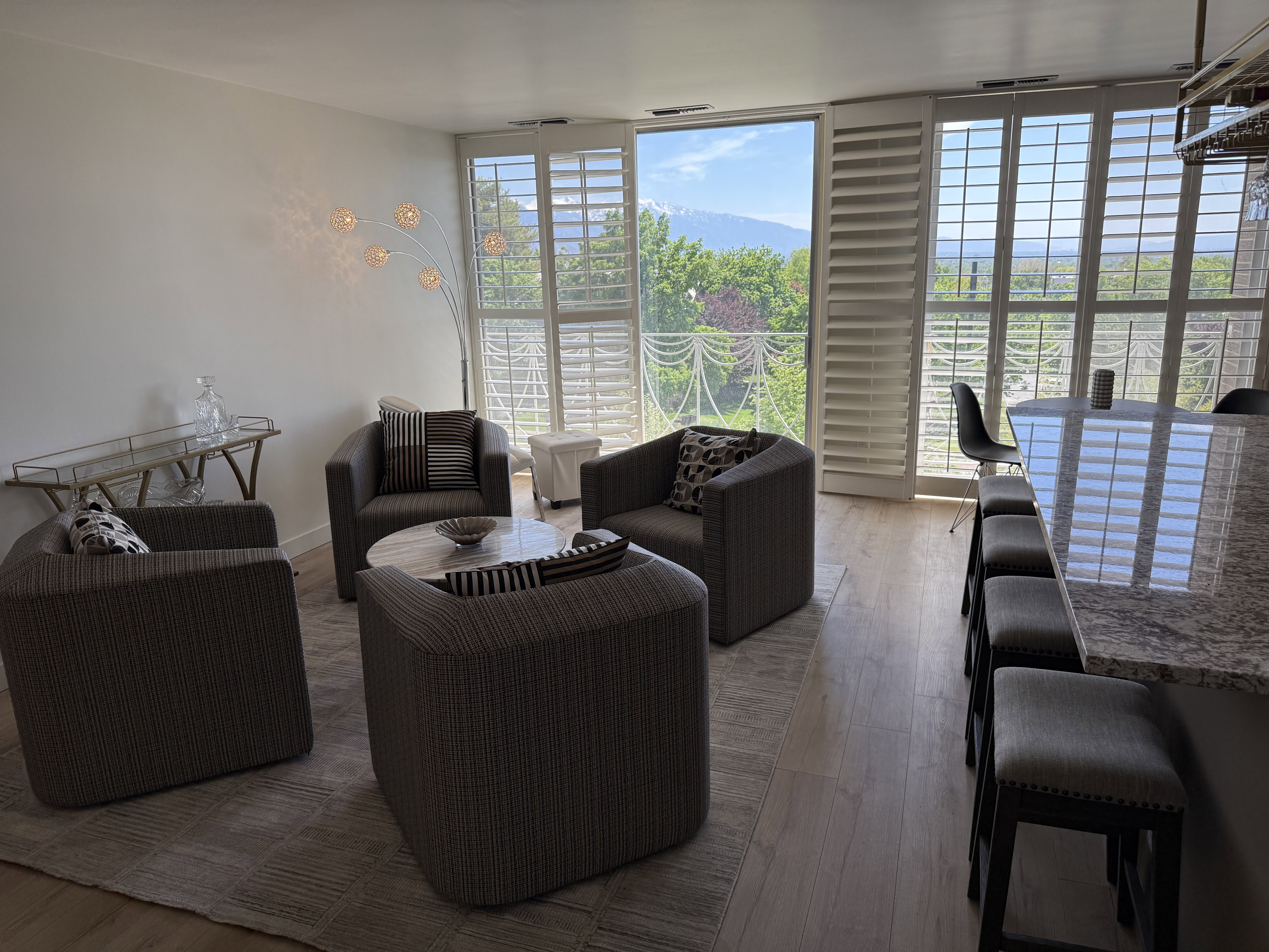 Living area featuring multiple large windows with plantation shutters, wood-finish flooring, and a kitchen island with a granite-look countertop