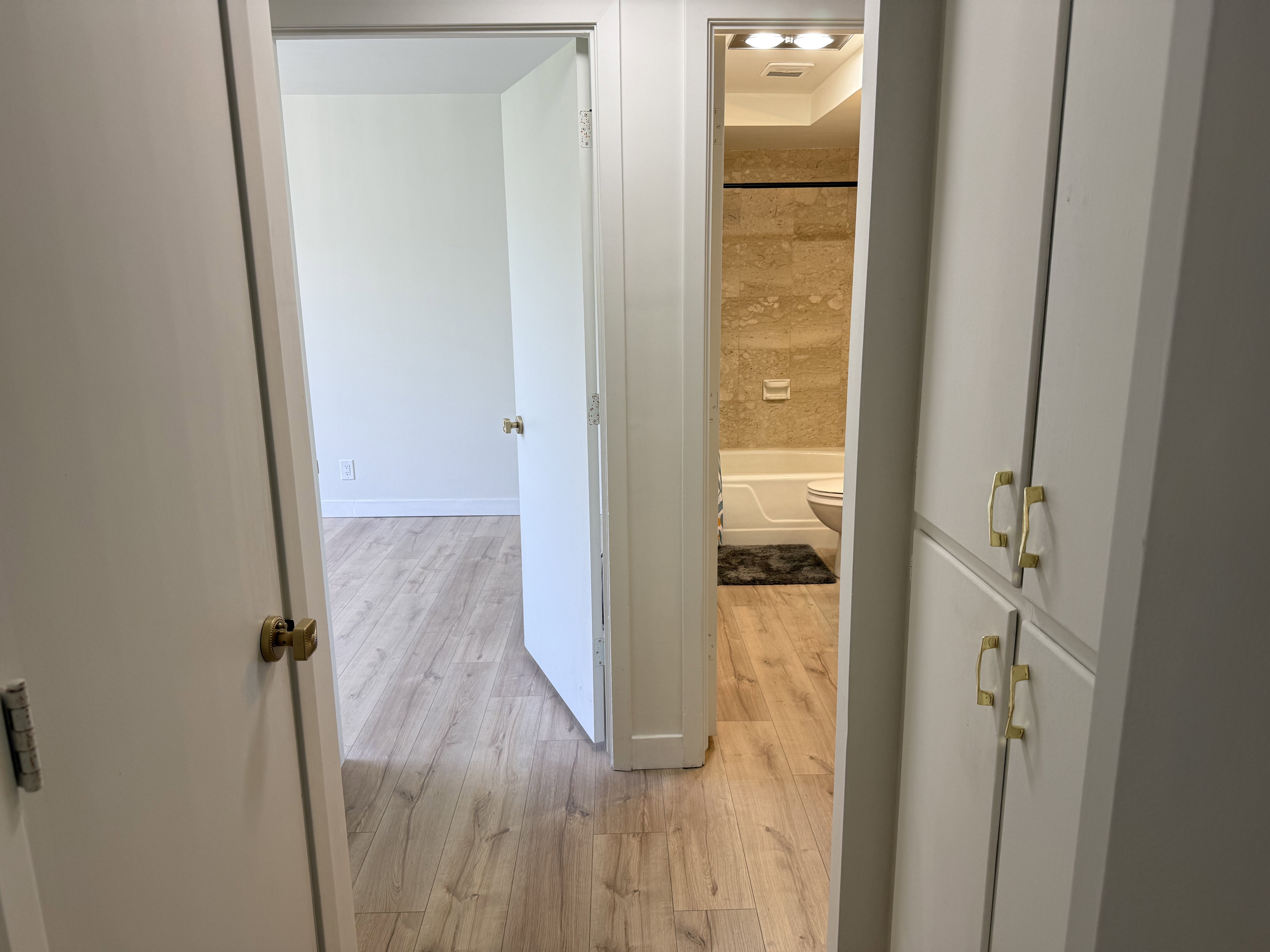 Hallway featuring wood-finish flooring, white walls, and built-in storage cabinetry with gold-tone hardware