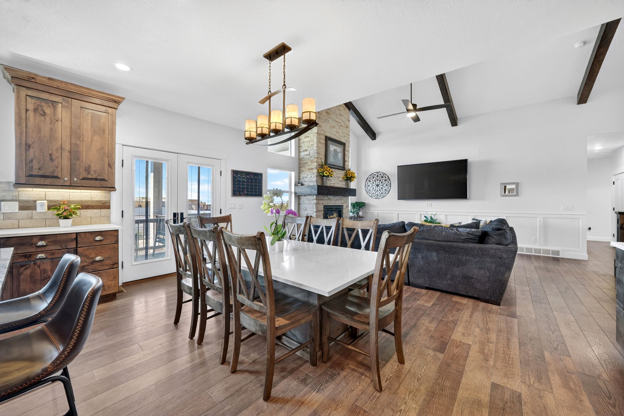 Open-concept living space featuring wood-finish flooring, a stone fireplace, and vaulted ceilings with exposed beams