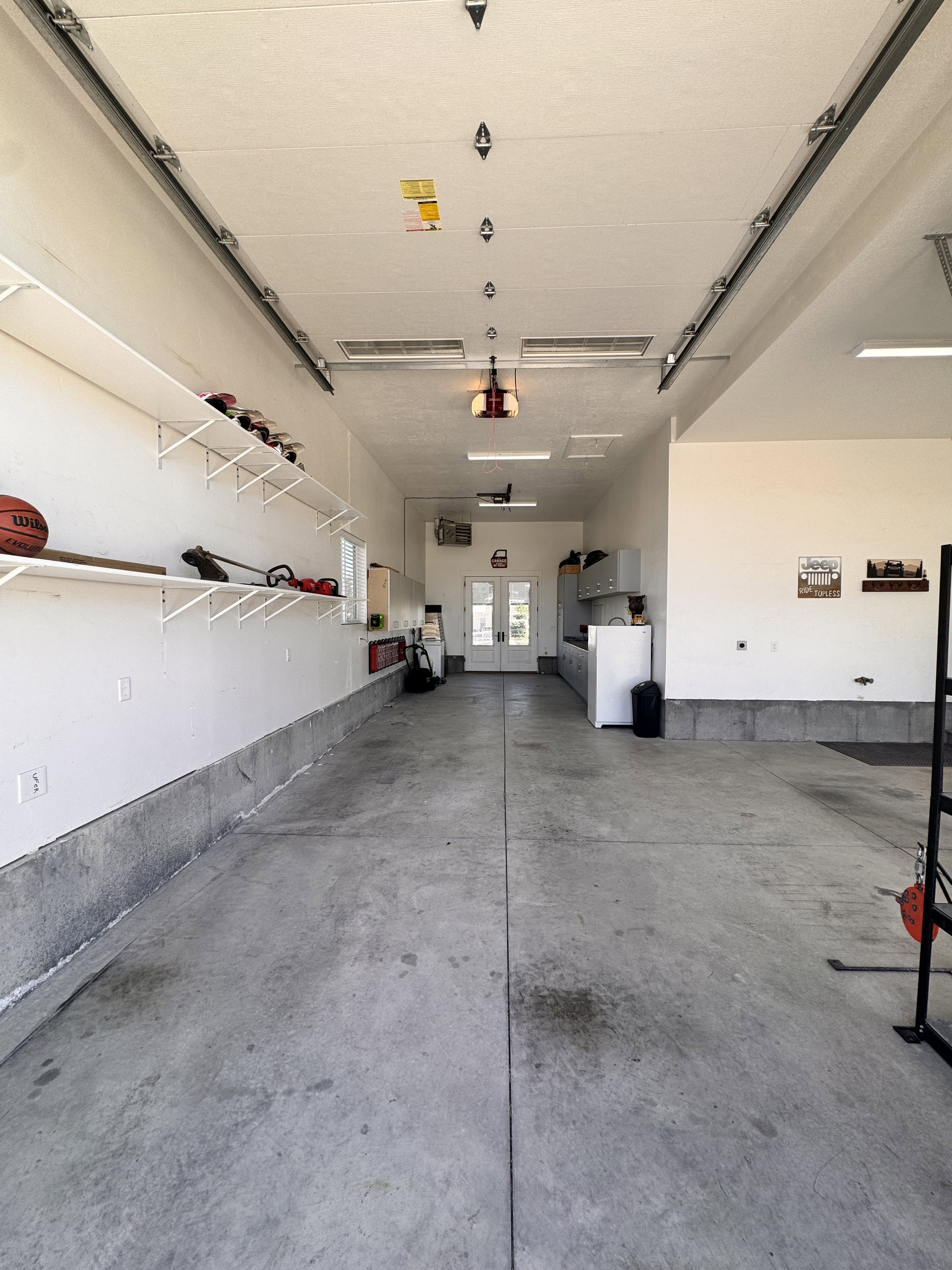 Spacious garage featuring a concrete floor, built-in shelving, overhead lighting, and white walls