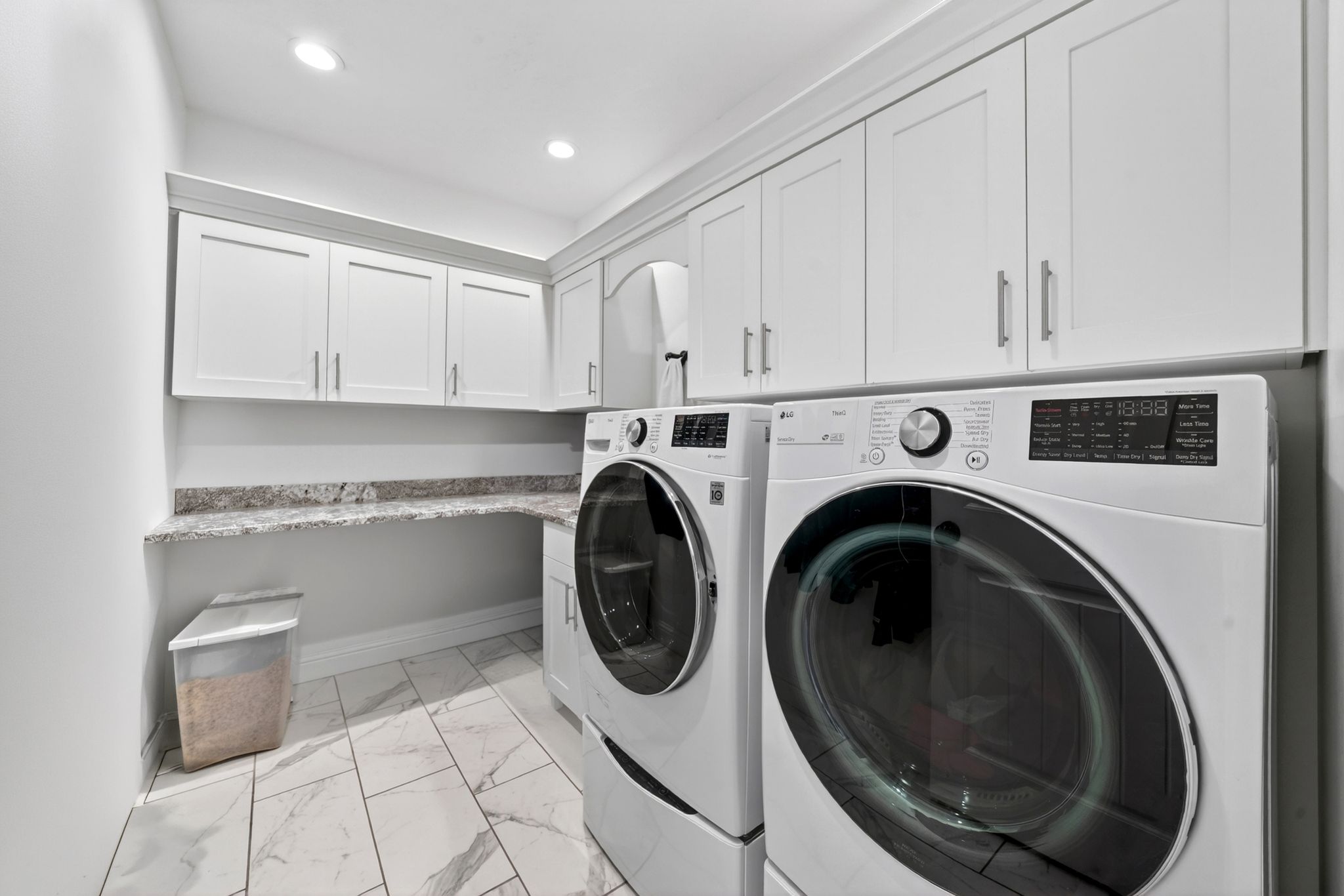 Dedicated laundry room featuring marble-look tile flooring, white shaker cabinetry, and a light-toned countertop