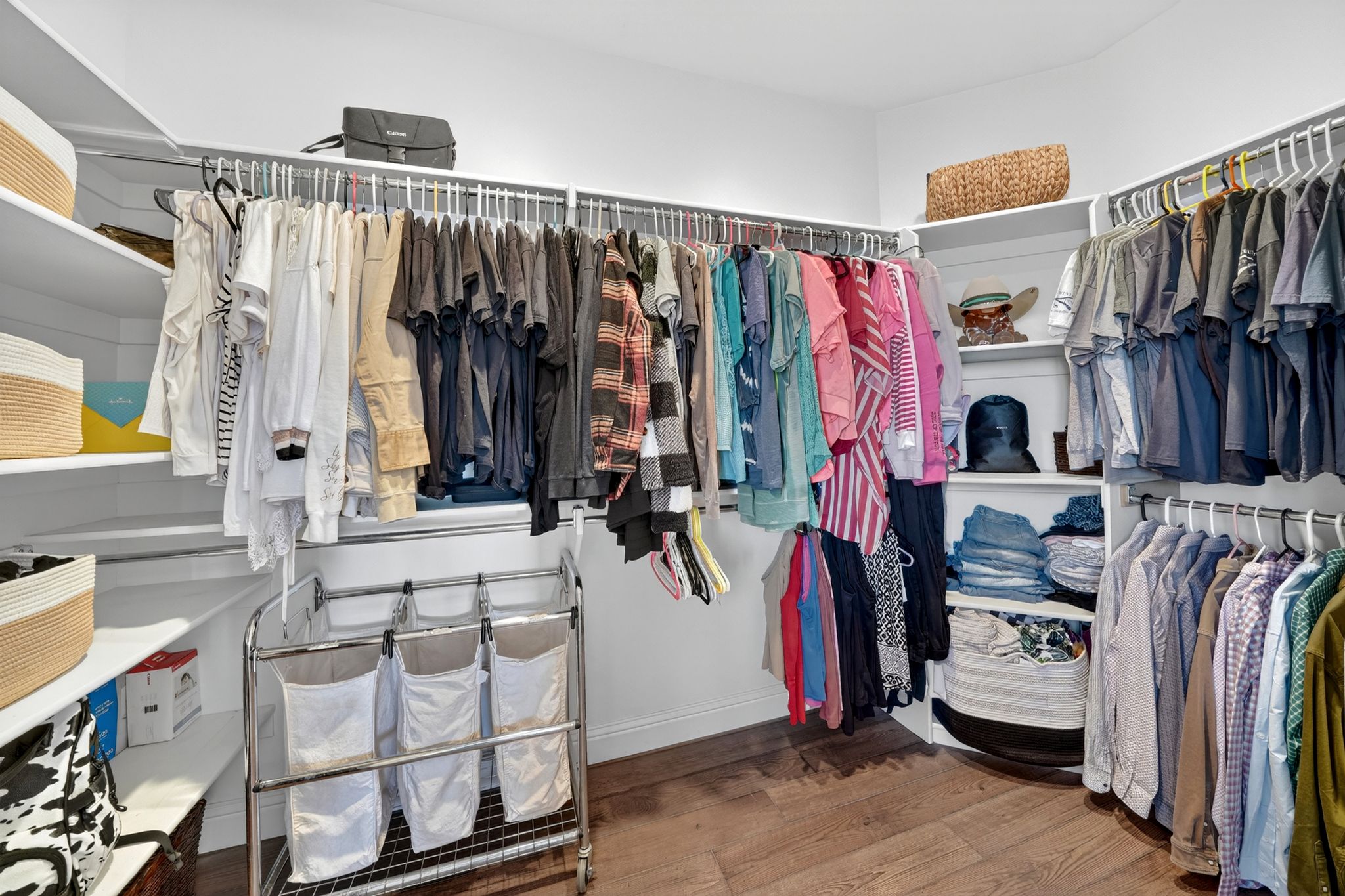 Spacious walk-in closet featuring white built-in shelving, multiple hanging rods, and wood-finish flooring