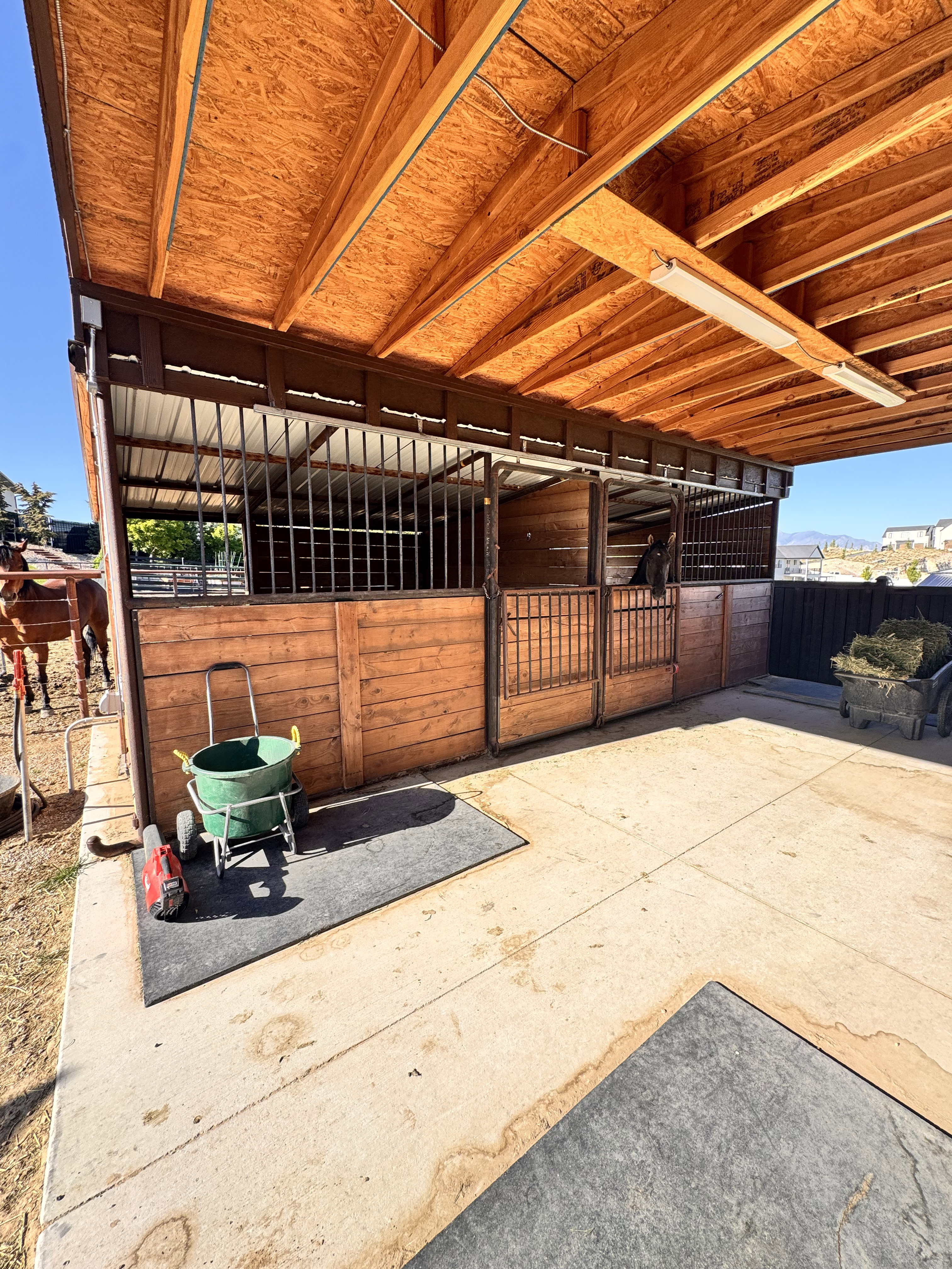 Covered equestrian facility featuring multiple wood-paneled stalls with metal grating