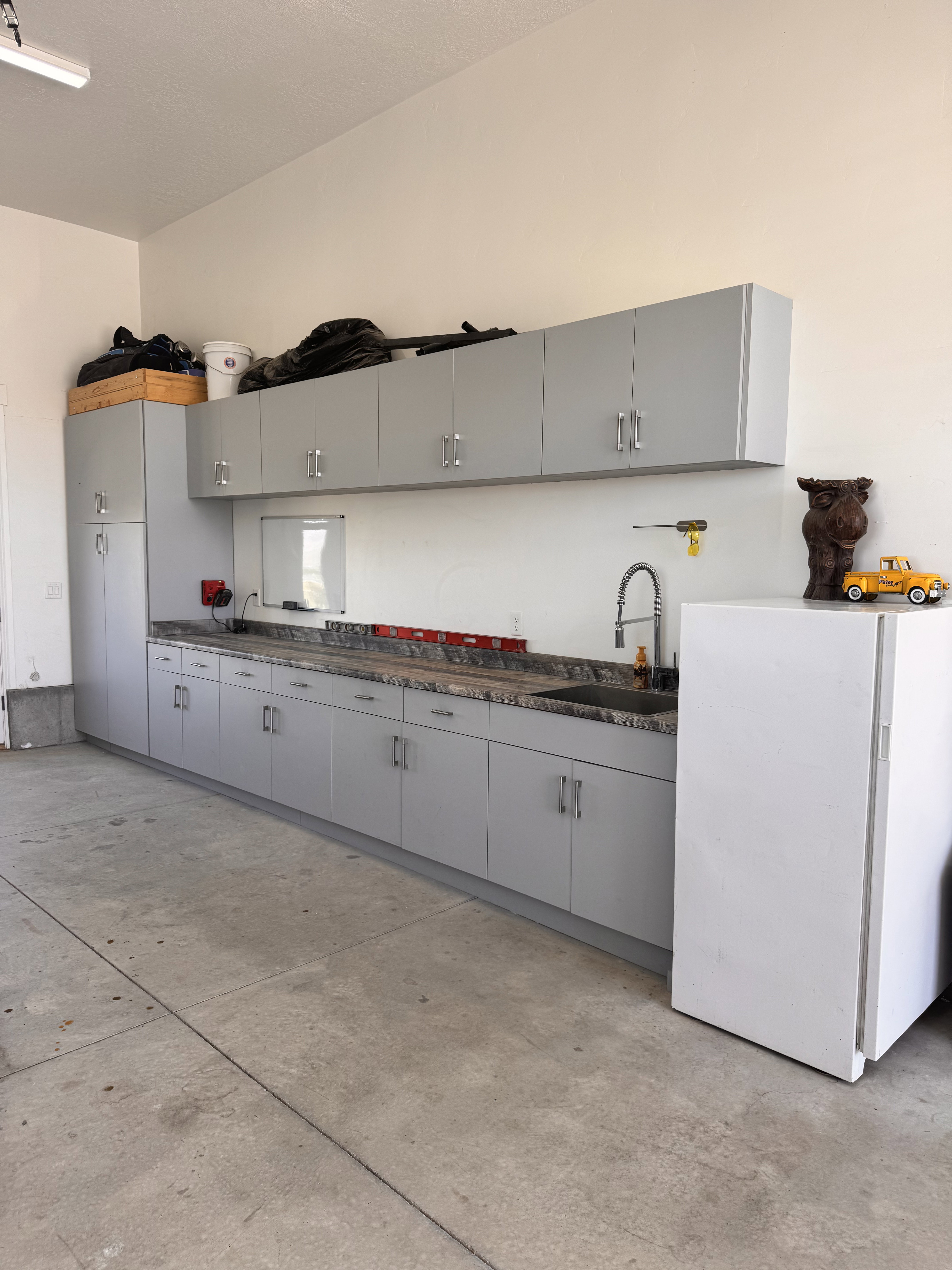 Garage workspace featuring extensive light gray cabinetry, a built-in sink with a gooseneck faucet, ample counter space, and a concrete floor