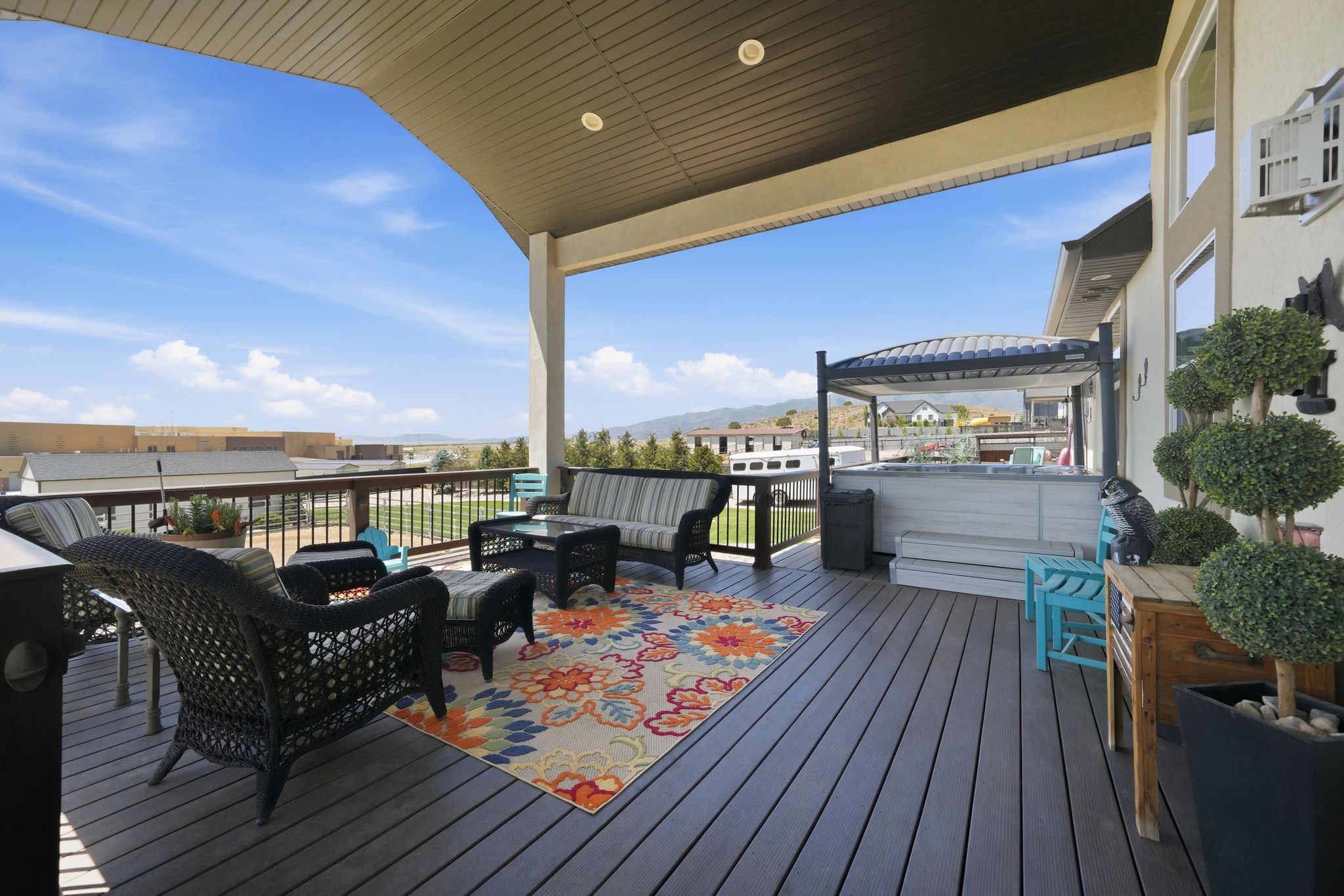 Spacious covered deck featuring composite decking, white siding, and a hot tub with an overhead pergola