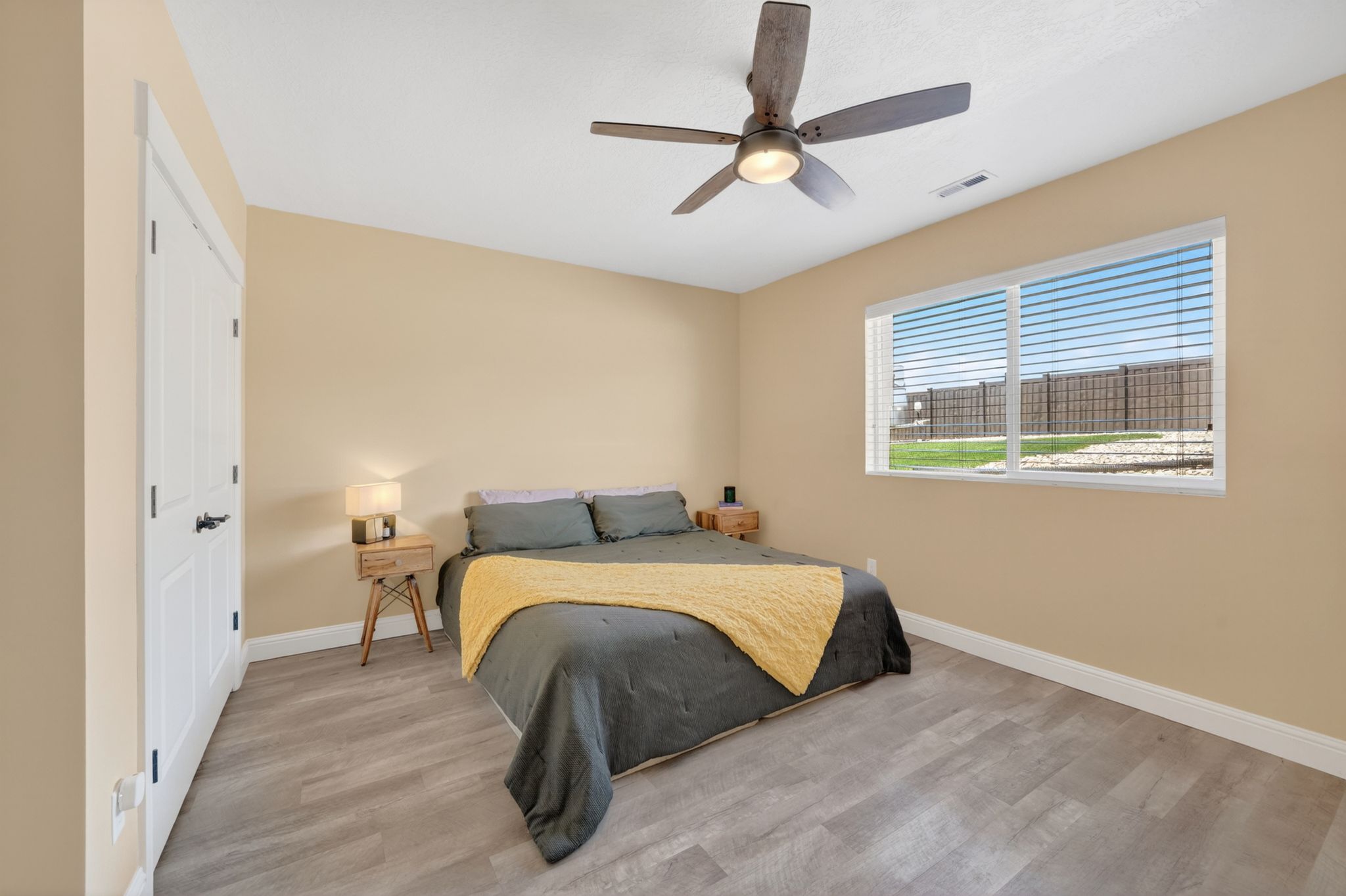 Spacious room featuring wood-finish flooring, a ceiling fan with integrated lighting, and a large window with blinds