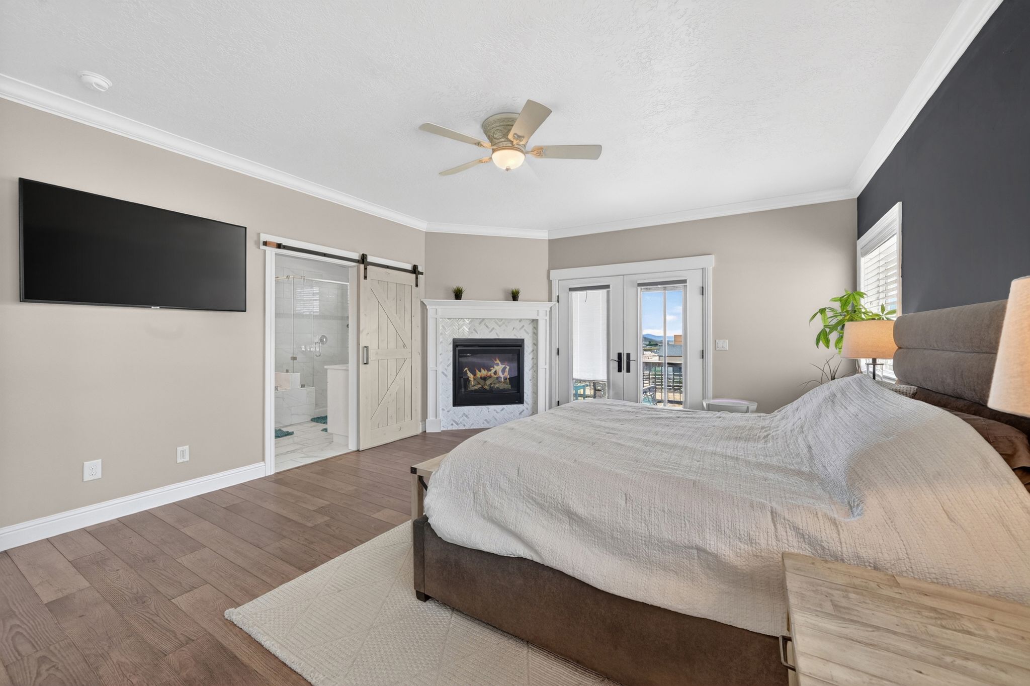 Spacious room featuring wood-finish flooring, a contemporary fireplace with a tiled surround, crown molding, and double doors opening to a balcony