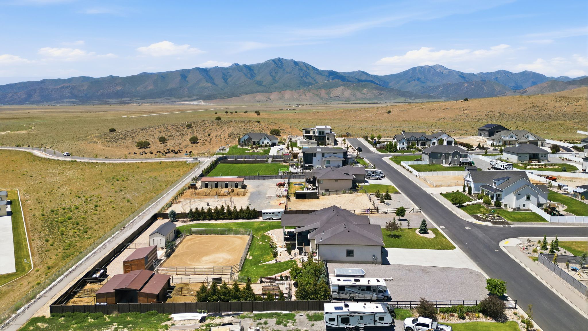 Expansive property featuring an outdoor riding arena, multiple outbuildings, and a gravel parking area, all set against a backdrop of distant mountains